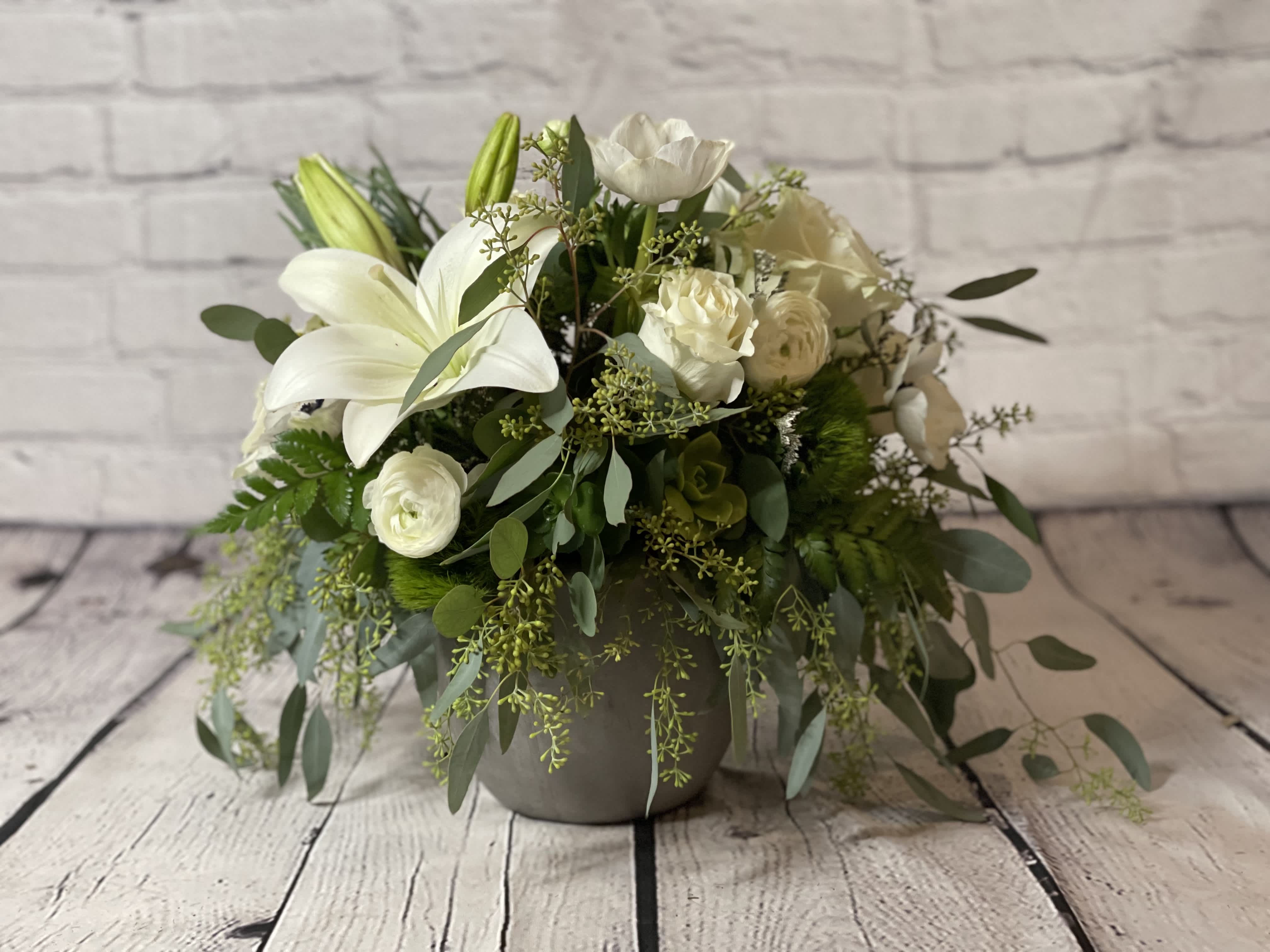 Beauty in White - Introducing &quot;Beauty in White&quot; - an enchanting floral arrangement crafted to captivate hearts and evoke a sense of ethereal elegance. This exquisite bouquet, showcased in a cement gray vase resting gracefully on a table, is a testament to nature's artistry.   At the heart of this stunning composition lie delicate white roses, exuding purity, and grace, their velvety petals gently unfurling in a mesmerizing dance. These pristine blooms are perfectly complemented by lush green leaves and an assortment of verdant greenery, creating a harmonious contrast that adds depth and dimension to the arrangement.   Ideal for a myriad of occasions, this floral creation makes for a captivating centerpiece at weddings, anniversaries, or even a charming gift to express your deepest sentiments. The serene white roses symbolize purity, innocence, and enduring love, making them a memorable choice for celebrations of love and new beginnings. 