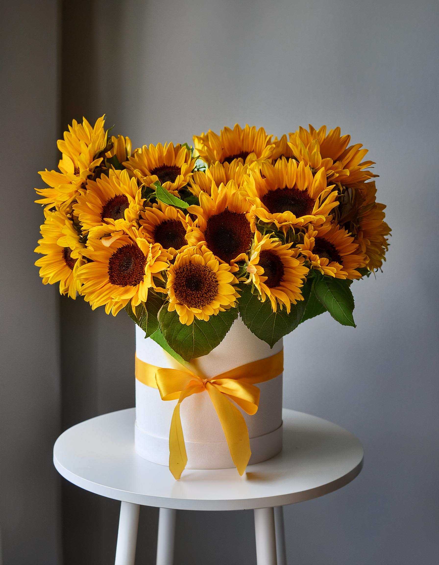Sunshine Bliss Sunshine Bliss - Celebrate life's special moments with our elegant white hatbox featuring radiant sunflowers. This stunning floral arrangement adds a touch of sunshine to your home or office. Ideal for gifting or self-indulgence