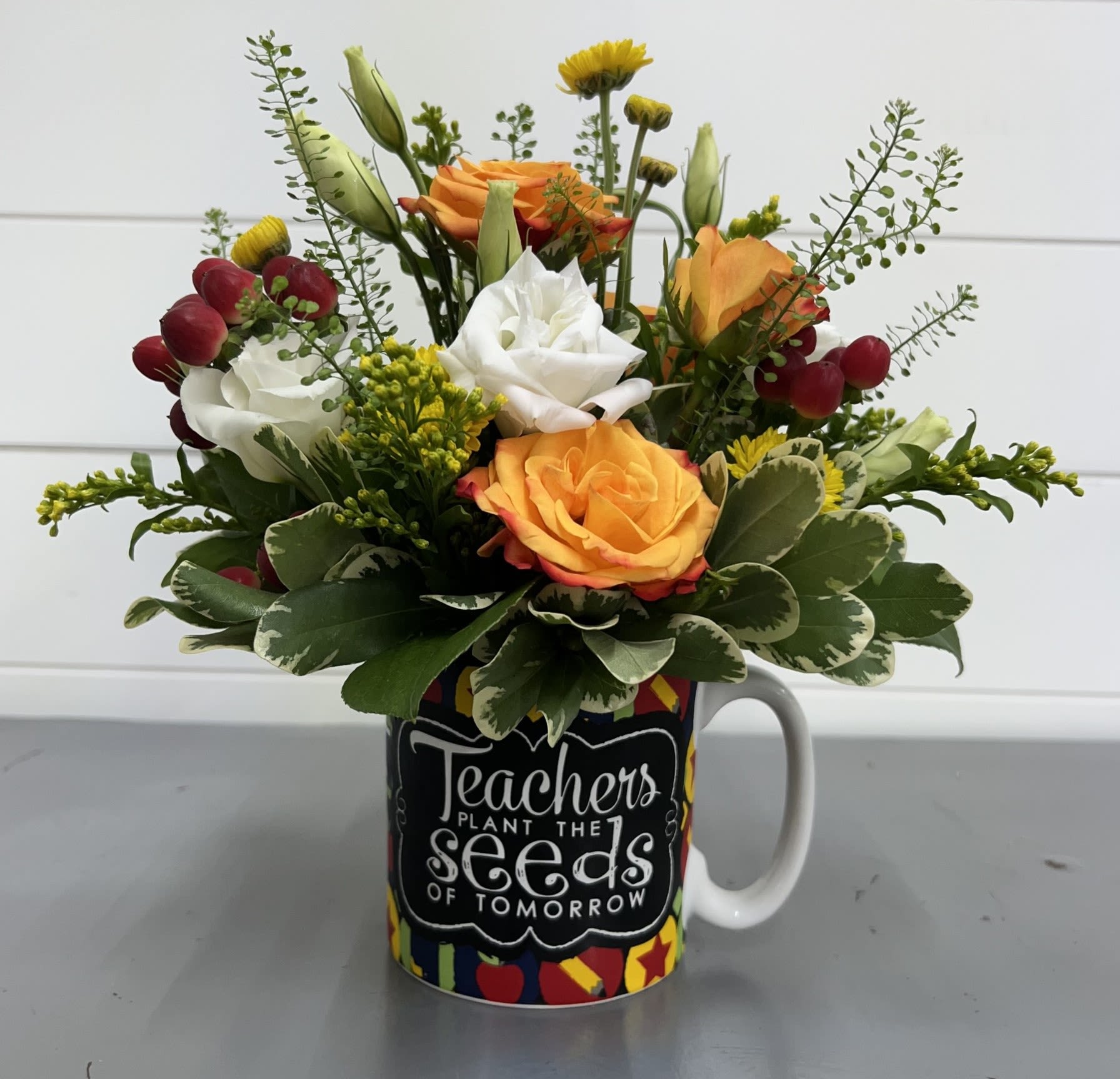 Teachers Plant The Seeds Of Tomorrow Teachers Plant The Seeds Of Tomorrow - Surprise your favorite teacher with this adorable keepsake mug filled with Orange Spray Roses, White Lisianthus, Yellow Buttons, Red Hypericum Berries and seasonal greenery.