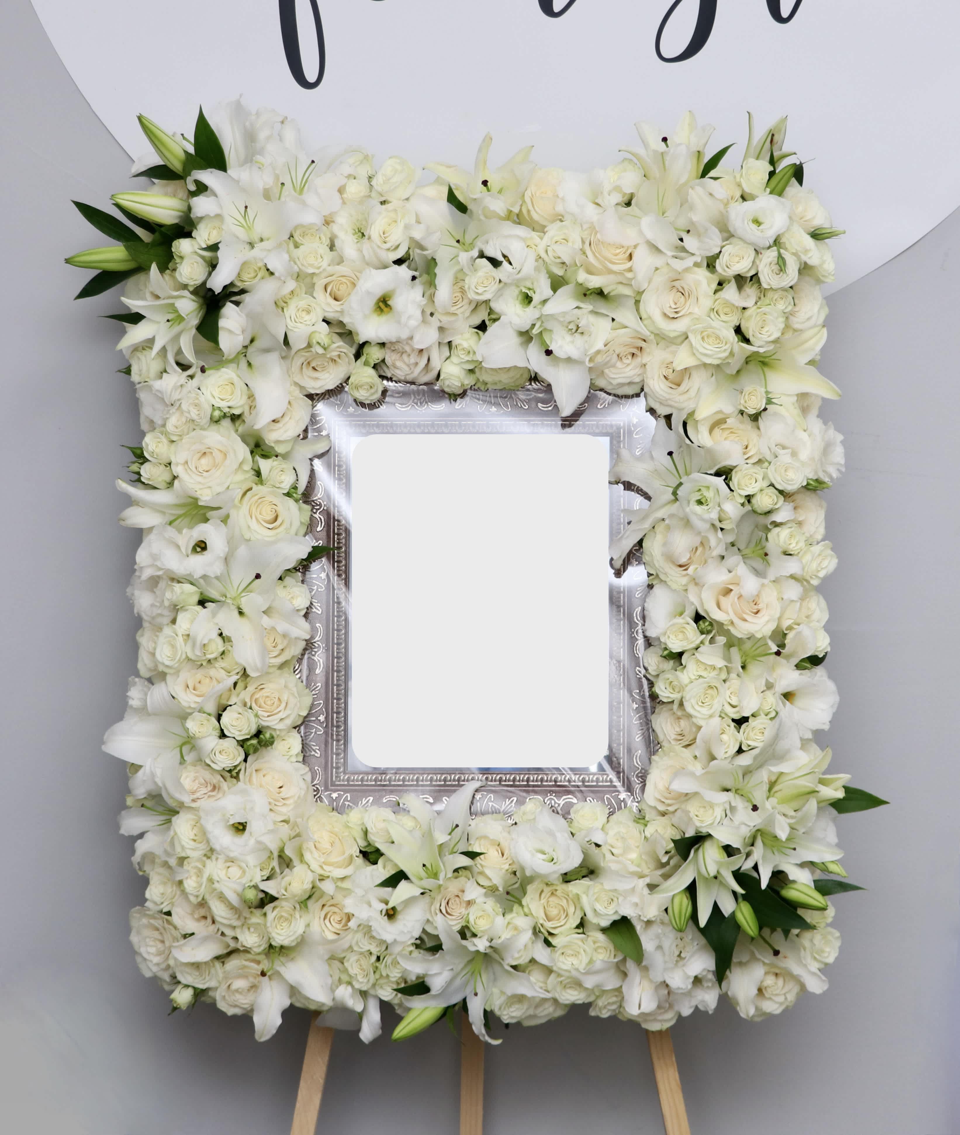White Lily Frame - This white sympathy frame is made with a variety of white florals including roses and fragrant casa blanca lilies.   Standard is about 32&quot; wide, deluxe 36&quot;, premium 42&quot;  11&quot; x 14&quot; frame is not included, please coordinate with us for drop off    We include easel, printed banner, and delivery (some fees may apply). An additional banner can be added for $15