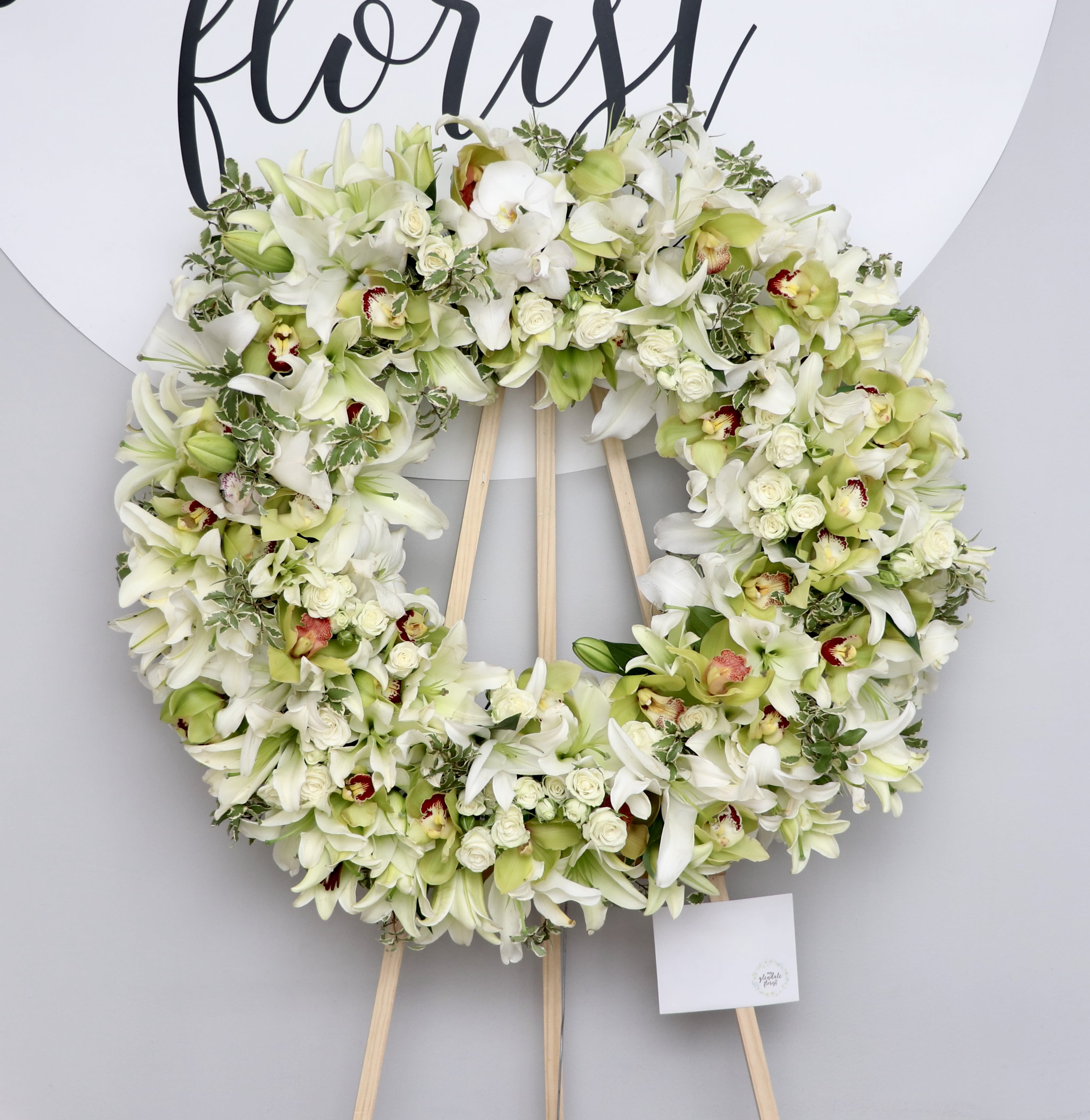 Lily and Orchid Wreath  - Lilies, Orchids, and spray roses make this the wreath anyone should get for a loved one.     We include easel, printed banner and delivery (some fees may apply). An additional banner can be added for $15    Standard size is 30'', deluxe is 36'', and premium is 42''.