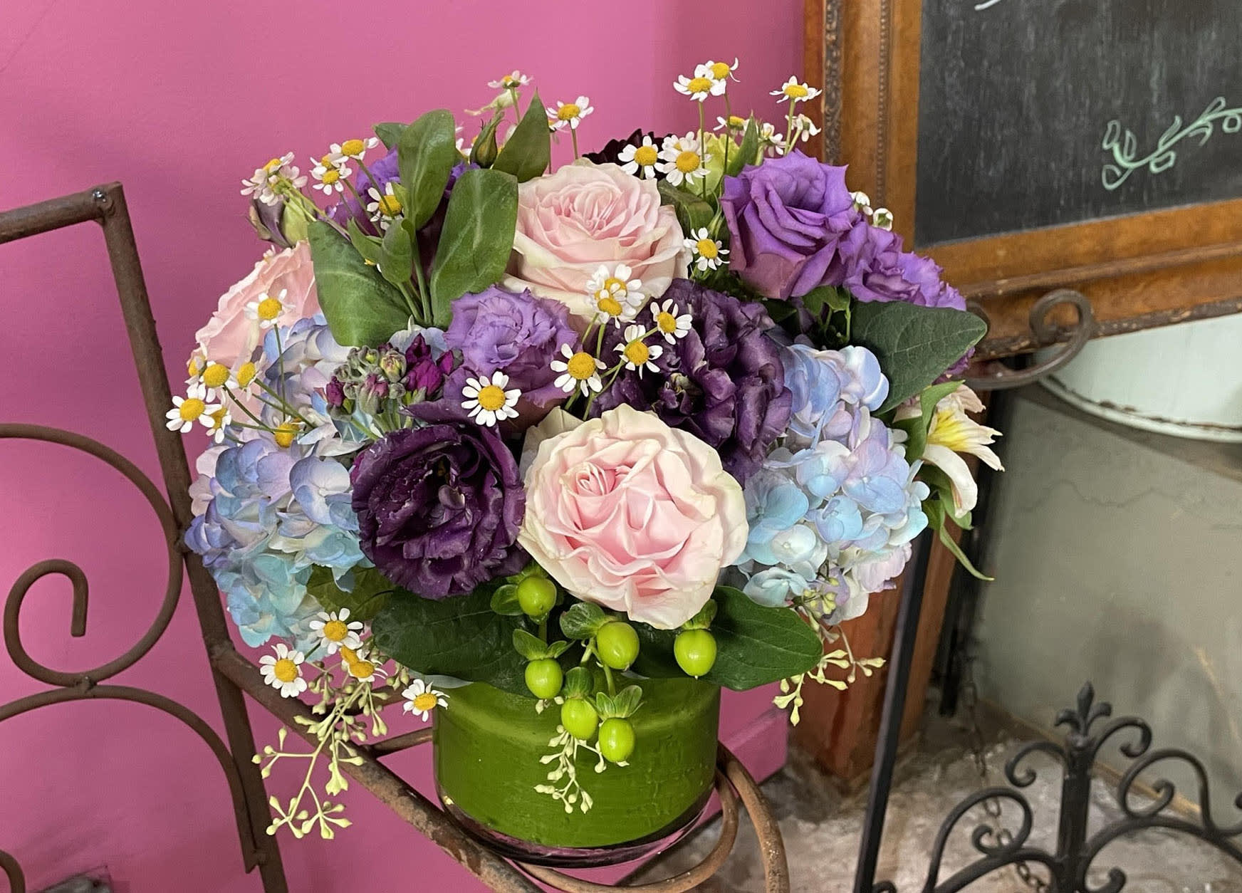 Constantina Constantina - Classic with a side of flair is what Constantina is all about. Flair up your order with features of purple lisianthus, orchids, green hypericum berries, lavender stock, and pink roses with chamomile accents. At approximately 11W x 12H in a 5 x 5 glass vase, no one is going to miss this beauty walking by.