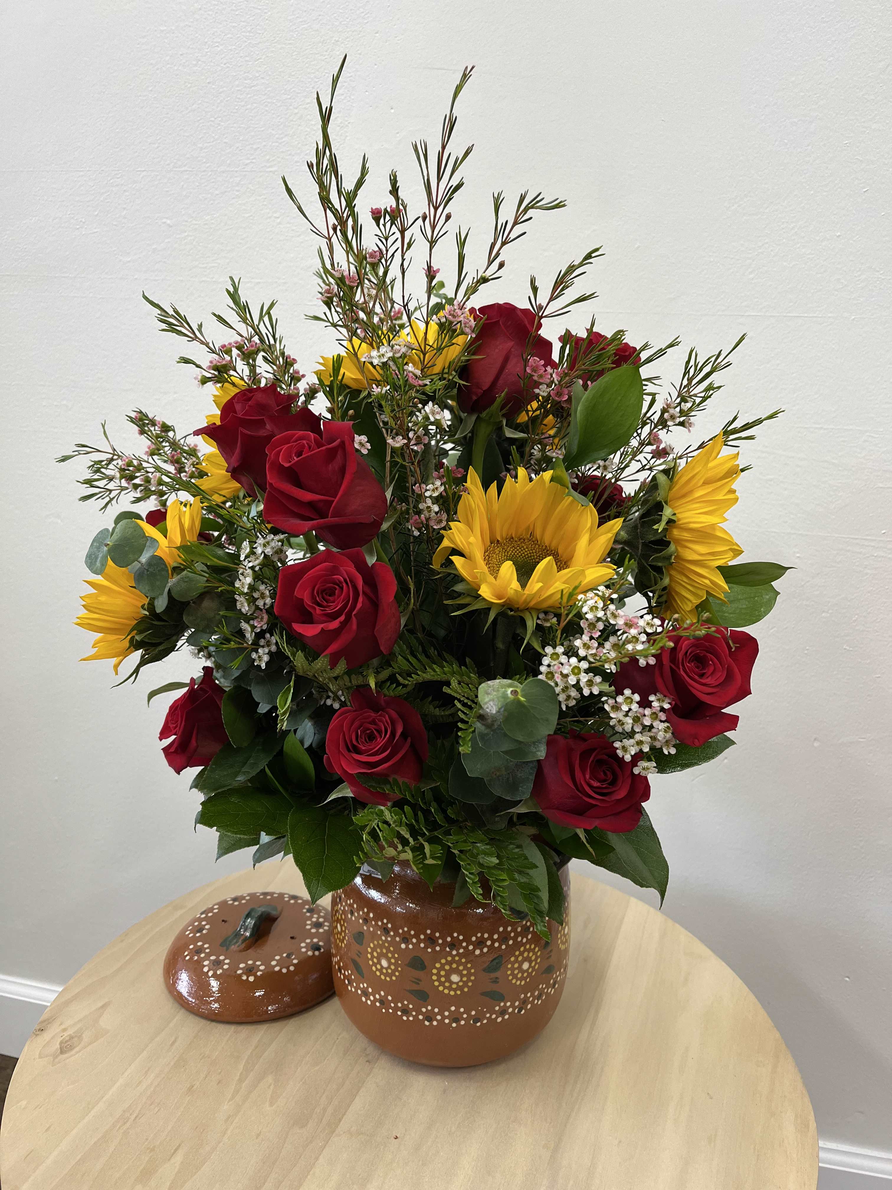 Encanto De Barro - “Encanto De Barro” charming arrangement of red roses, vibrant, sunflowers, and lush greenery beautifully presented in rustic clay pot. Perfect for adding a touch of natural elegance to any space.