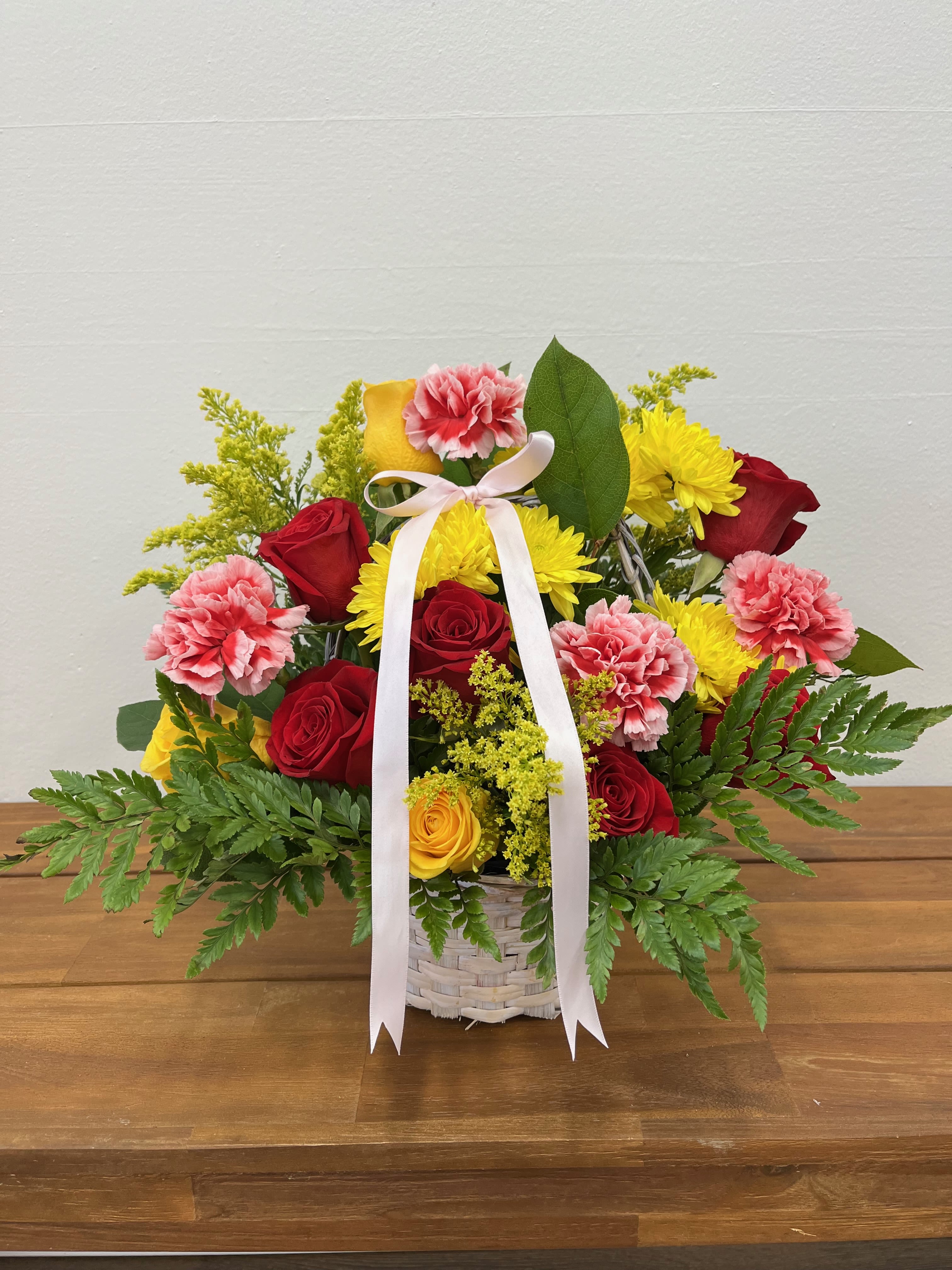 Garden Delight  - This arrangement has a classic beauty of red and yellow roses with the cheerful tones of pink and yellow carnations. Accented by delicate limonium and lush baker greenery, all nestled in a white basket adorned with a matching bow, this bouquet exudes elegance and joy