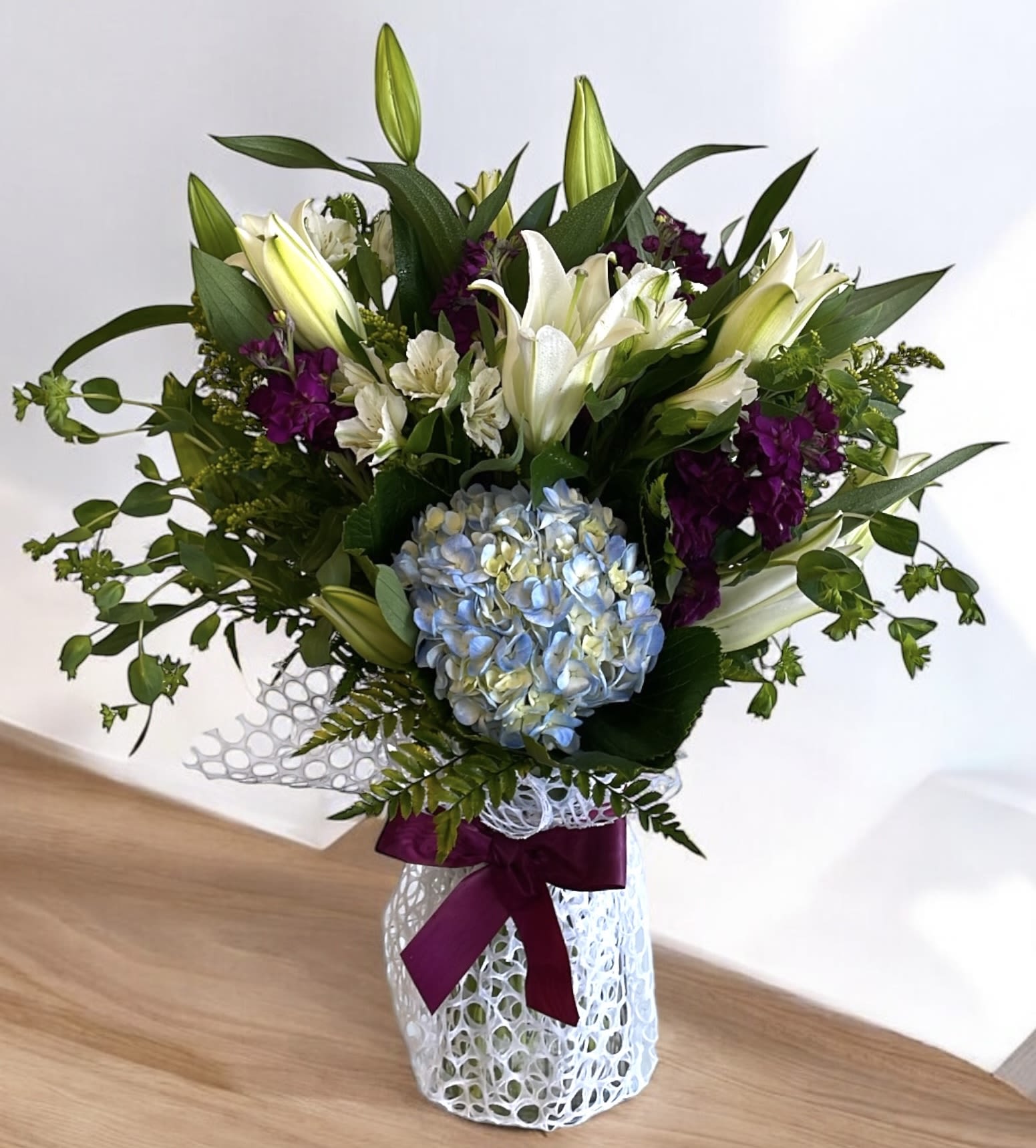 Breezy by the Sea by BloomNation™ Breezy by the Sea by BloomNation™ - This arrangement contains delphinium, bells of ireland, asiatic lilies, hydrangea, blue iris, mokara orchids, and other seasonal blooms. It is a great gift for a birthday, get well, for wishing someone a fresh start. APPROXIMATE DIMENSIONS: 15" D x 18" H