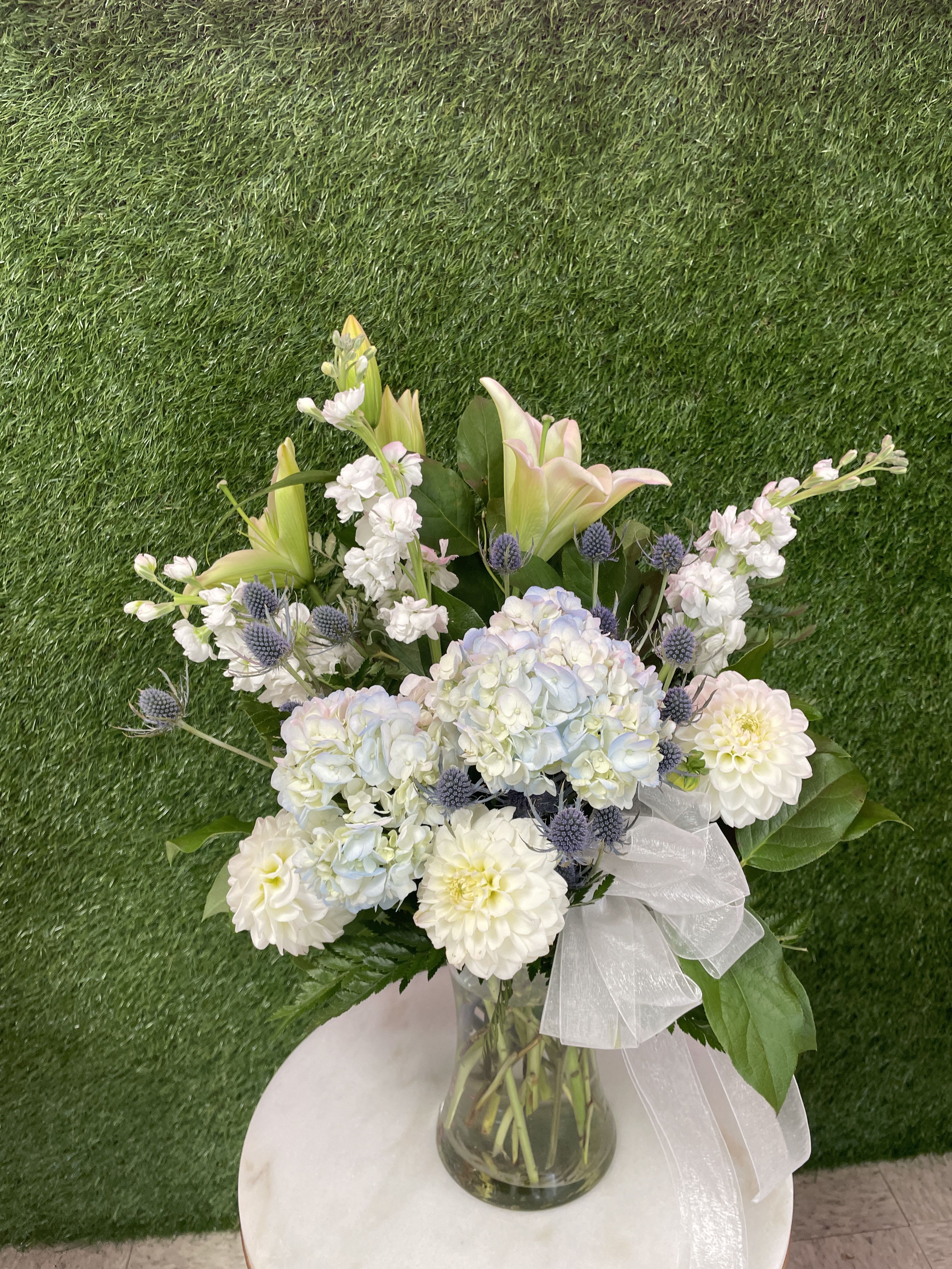 Heavenly Blue Heavenly Blue - Sympathy arrangement with a mixture of blue and white flowers with a white sheer bow.