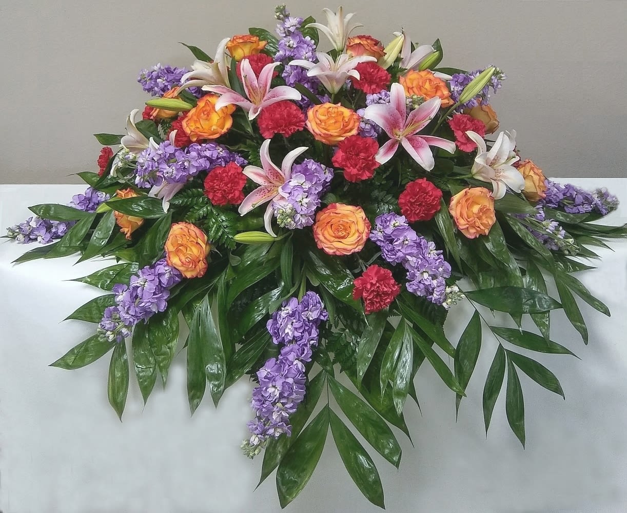 Casket Spray of Bright Shades Casket Spray of Bright Shades - Casket spray of lavender stock, confetti roses, stargazer lilies, and red carnations.