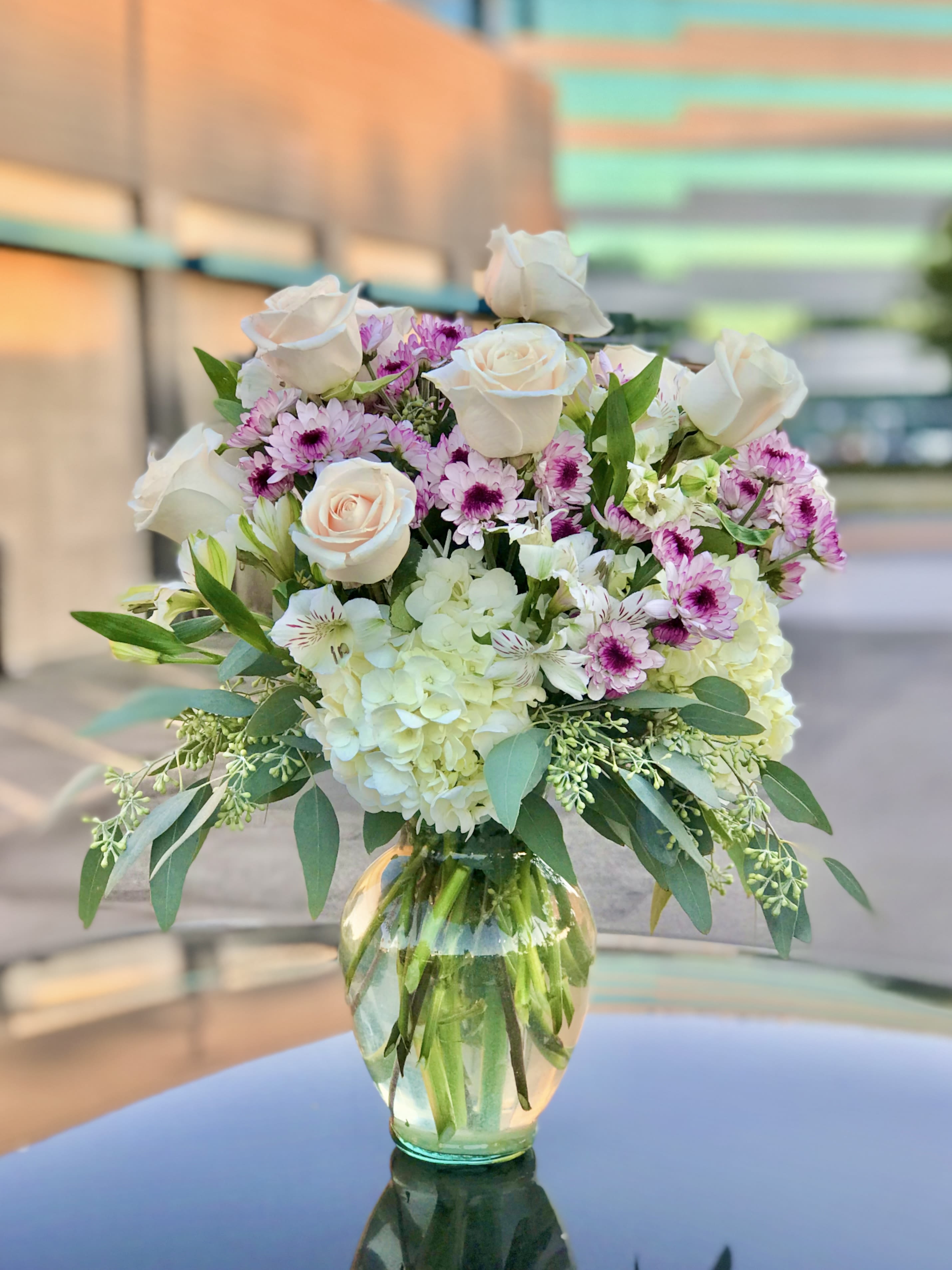 With Grace - Send your loved one this beautiful arrangement made with premium roses, beautiful fluffy hydrangea and color popping mums. All fresh flowers are in a 9.5 inch clear glass vase. 