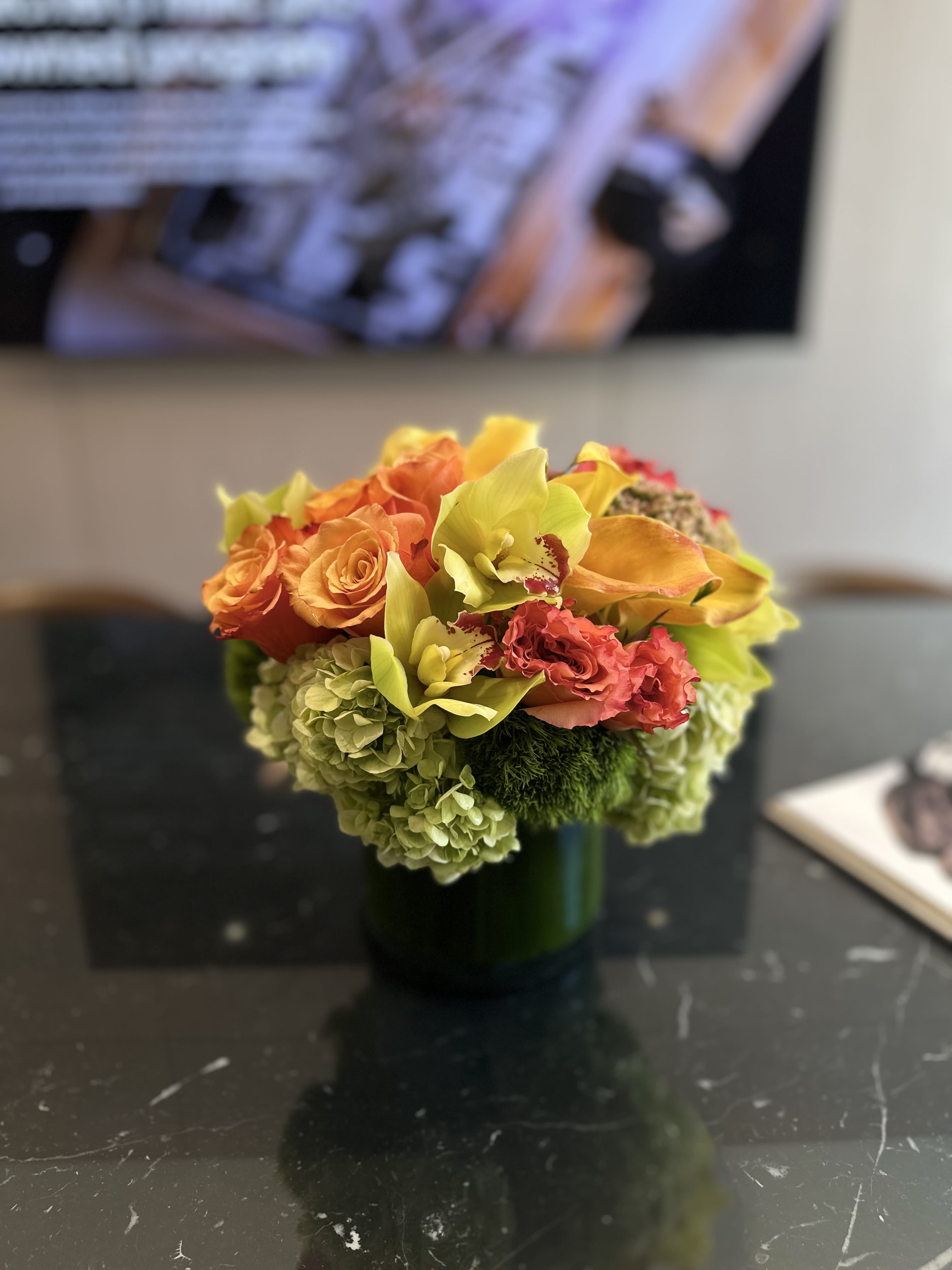 Fyre - Introducing &quot;Fyre,&quot; a radiant floral arrangement that dazzles with its fiery blend of fresh, high-quality flowers. Bursting with vibrant orange roses, vivid yellow orchids, and lush green hydrangeas, this bouquet is a celebration of color and texture. Each flower is carefully selected for its freshness and longevity, ensuring that &quot;Fyre&quot; maintains its stunning appearance for as long as possible. Perfectly contained in a sleek green vase, this arrangement not only adds a burst of energy to any space but also exudes a sense of luxury and vitality. Ideal for brightening homes or offices, &quot;Fyre&quot; is designed to capture the essence of dynamic beauty and freshness.