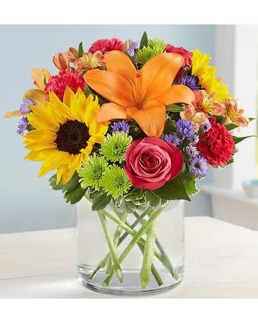 Floral Embrace - This colorful bouquet is just as special as giving someone a hug in person! Crafted by our expert florists from a vibrant gathering of blooms a classic cylinder vase, its beauty and charm will help you express yourself perfectly, no matter how far apart you are. All-around arrangement of hot pink roses and carnations; orange Asiatic lilies and Peruvian lilies (alstroemeria); yellow sunflowers; lavender stock; purple monte casino; green Athos poms; accented with assorted greenery To ensure lasting beauty, lilies may arrive in bud form, and will fully bloom over the next few days Our florists hand-design each arrangement, so colors, varieties and container may vary due to local availability Artistically designed in a glass vase Premium arrangement does not include carnations; measures approximately 13&quot;H x 13&quot;L; vase measures 6&quot;H Deluxe arrangement; measures approximately 12&quot;H x 12&quot;L; vase measures 5&quot;H Standard arrangement does not include stock; measures approximately 11&quot;H x 11&quot;L; vase measures 5&quot;H