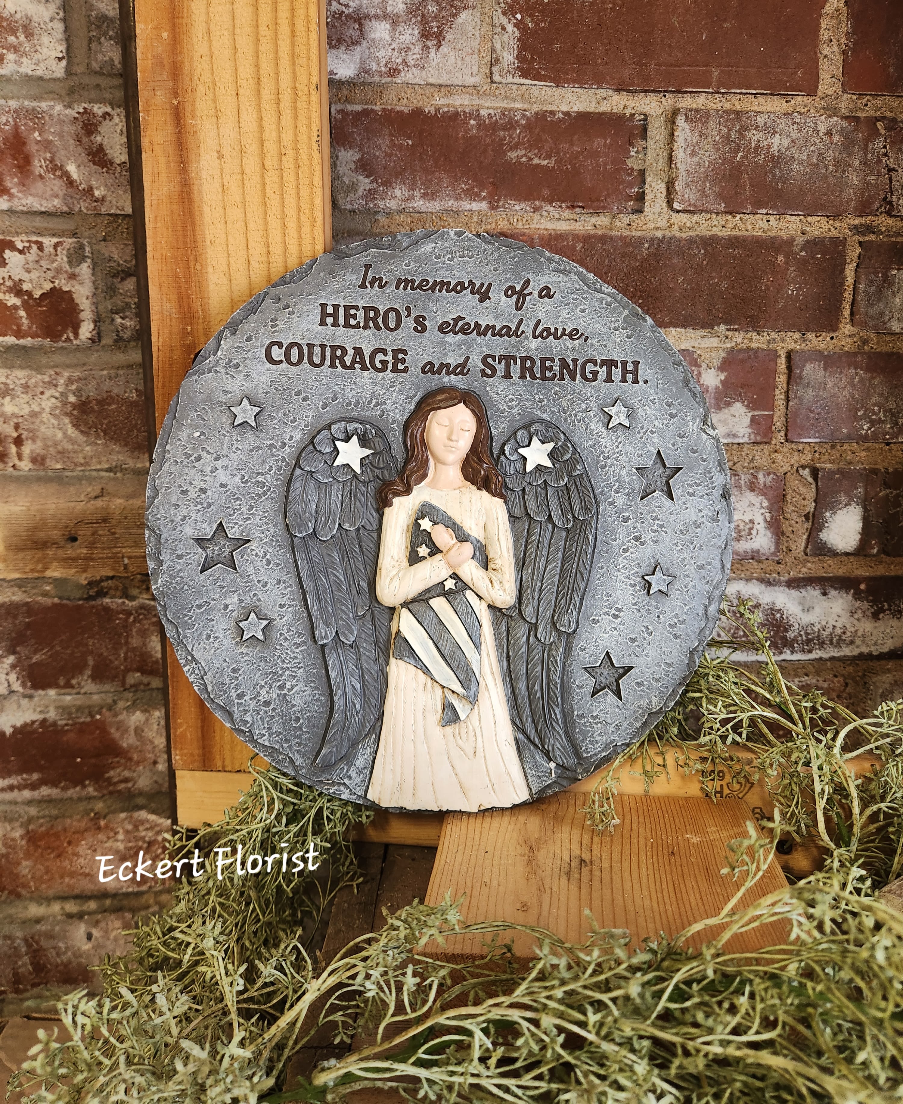 Eckert Florist's "In Memory Of A Hero..." Memorial Stone *Our Local Deliery Only Eckert Florist's "In Memory Of A Hero..." Memorial Stone *Our Local Deliery Only - Resin stone measures approx. 10.5" Diameter This nice memorial keepsake may be sent to a funeral/memorial service or home. Can be added to a green plant or fresh arrangement. See Deluxe or Premium upgrades. Sentiment: "In memory of a Hero's eternal love, Courage and Strength" *See Add-on Section for Display Easel *LOCAL DELIVERY ONLY