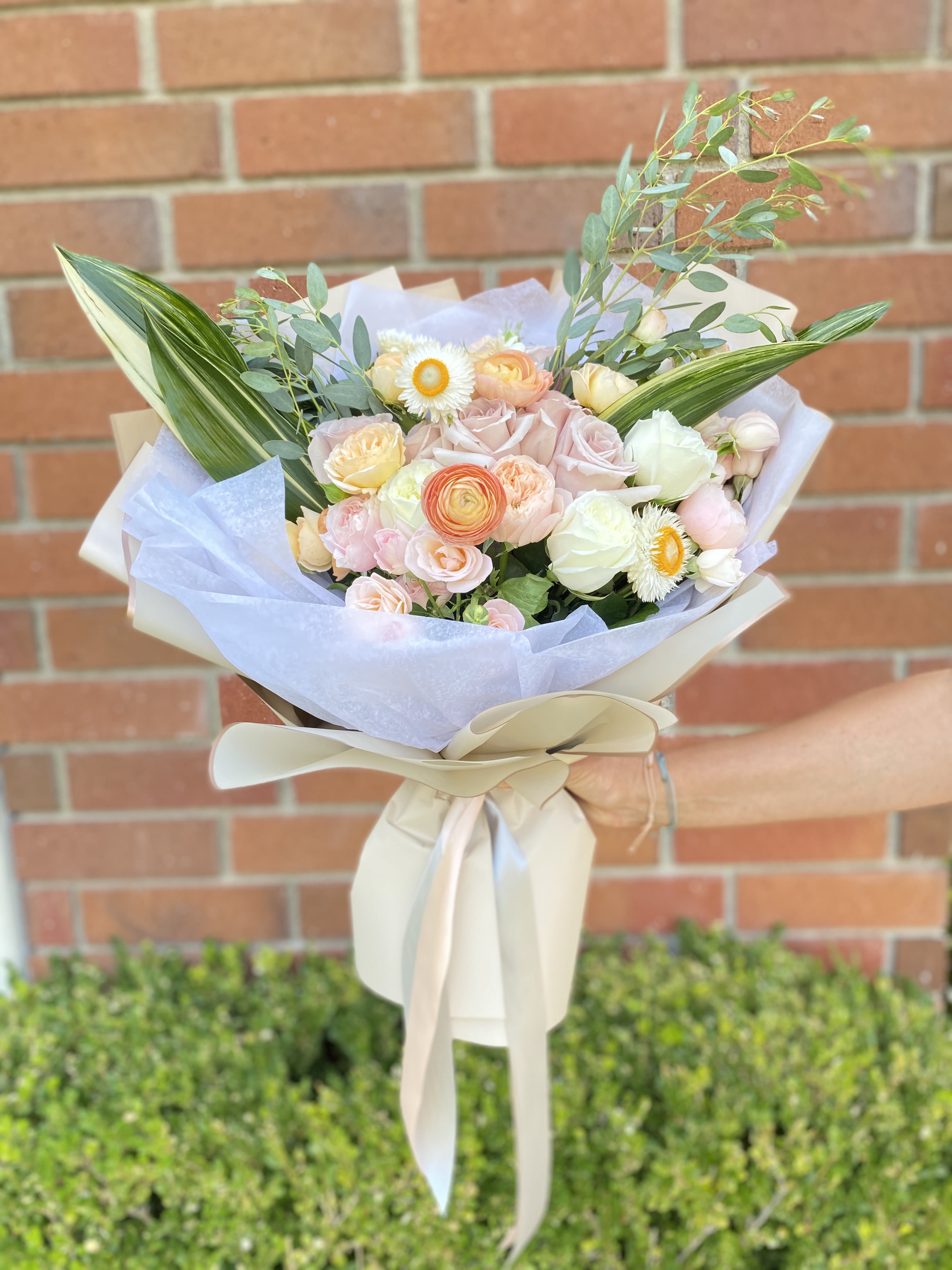 Peach Perfect - Beautiful peach and light pink blooms with the perfect amount of greens wrapped in multiple layers of delicate waterproof paper and a doubled sided satin ribbon. 
