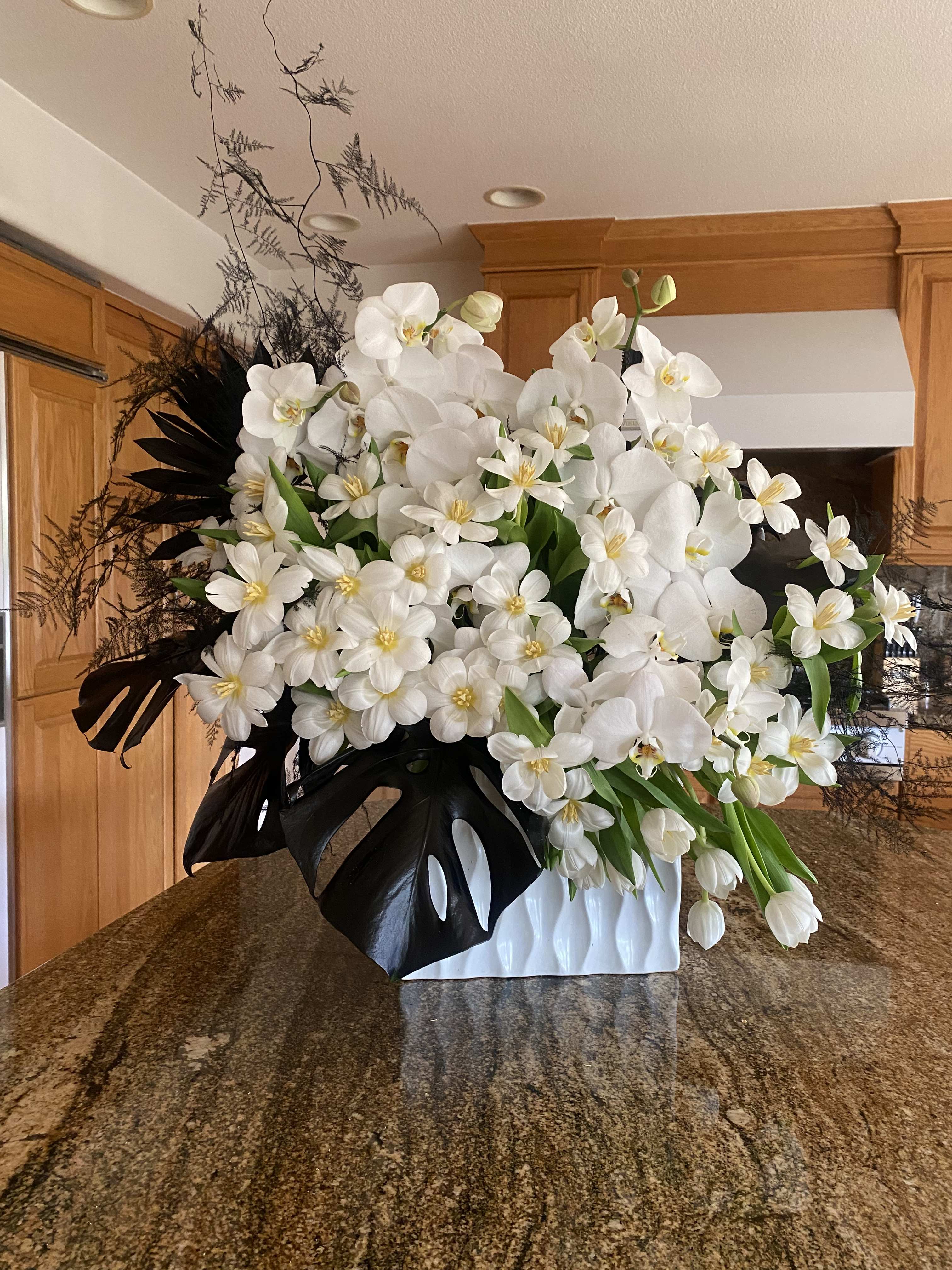 White and Black Garden White and Black Garden - This beautiful white orchids and tulips arrangement is the perfect gift to impress anyone. The perfect amount of black greenery makes a dramatic contrast against the cascading white flowers.