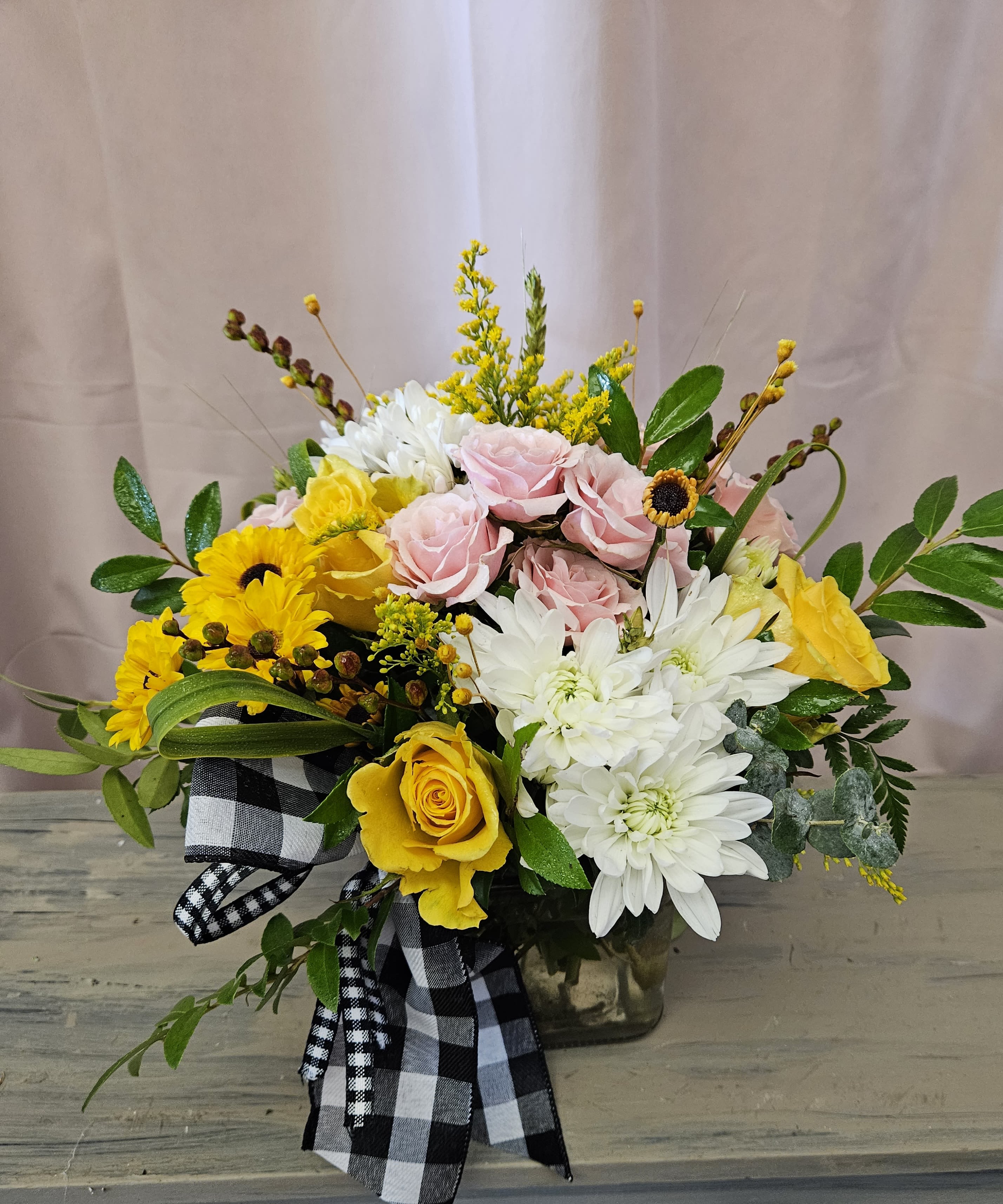 The Effie The Effie - Sweet and charming cube vase arrangement with yellow daisies, white mums, yellow and pink roses and wildflower accents.