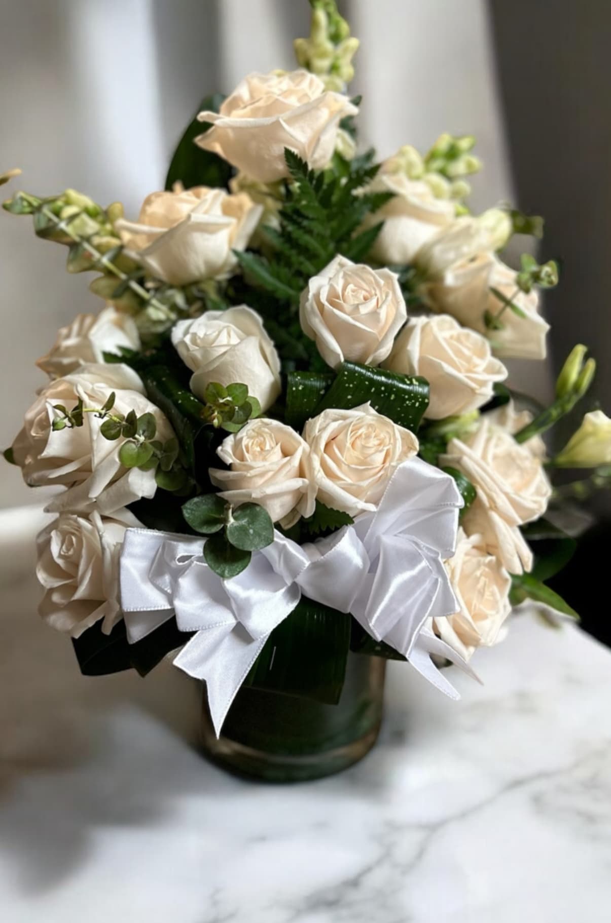 Elegant Lady Elegant Lady - A dozen white rose arrangement designed with Tea leaves and Eucalyptus. Adorned with a white bow in glass vase. A very elegant arrangement for any occasion.