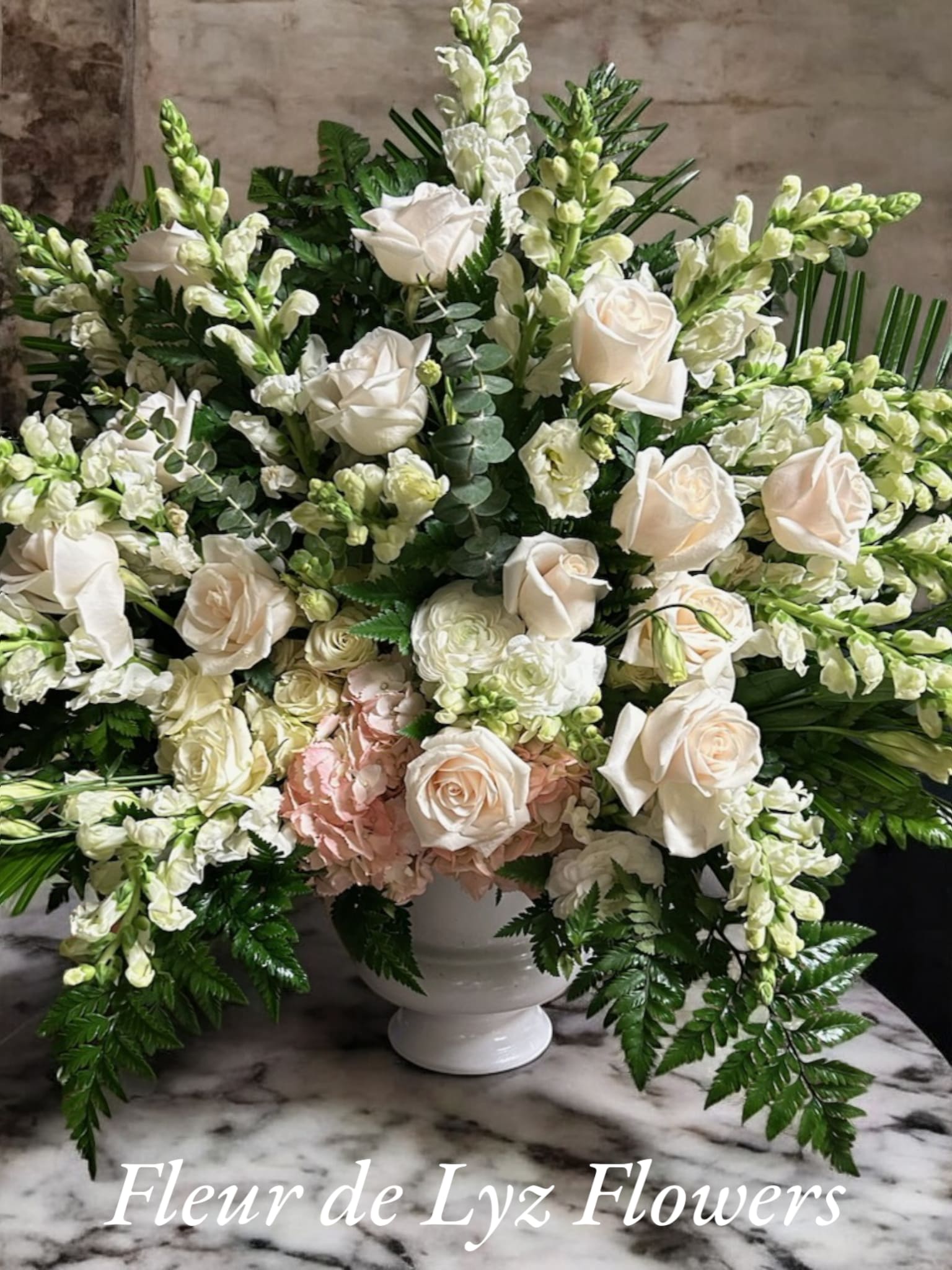 Peace and Serenity Peace and Serenity - This Elegant Sympathy arrangement is designed with White roses, Snap Dragons and Hydraengeas. Palm leaves, Leather leaf and Eucalyptus in a white vase container.