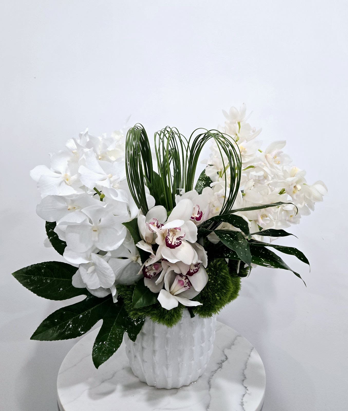 Orchid Whisper - Modern and sleek collection of assorted white orchids, and lush greenery in a textured white vase, perfect for a minimalist yet elegant look.
