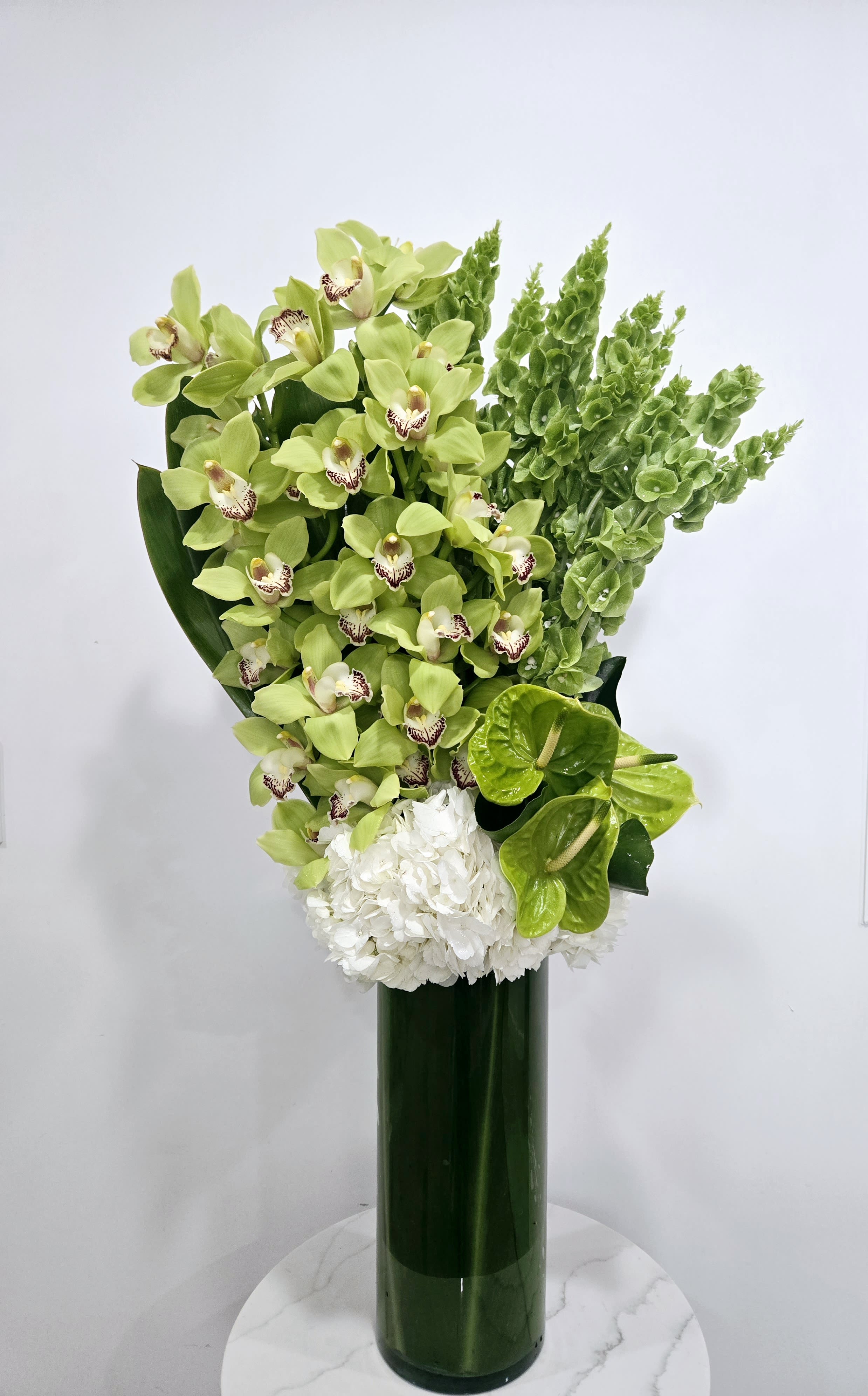 Green Orchids - Tall arrangement in glass cylinder composed of green cymbidium orchids, white hydrangeas and green bells of Ireland. 