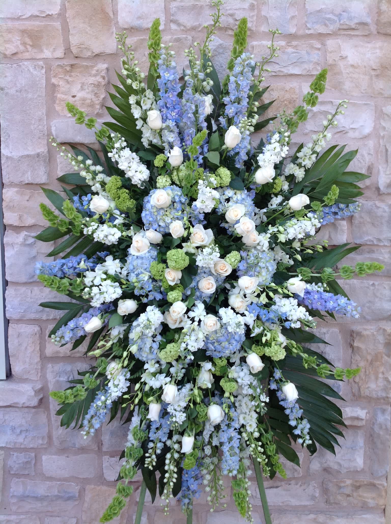 Blue Standing Spray  - This beautiful mostly Blue standing spray includes Hybrid Delphinium, Delphinium, Hydrangea's, Bells of ireland, Stock, Roses, and Dendrobium Orchids