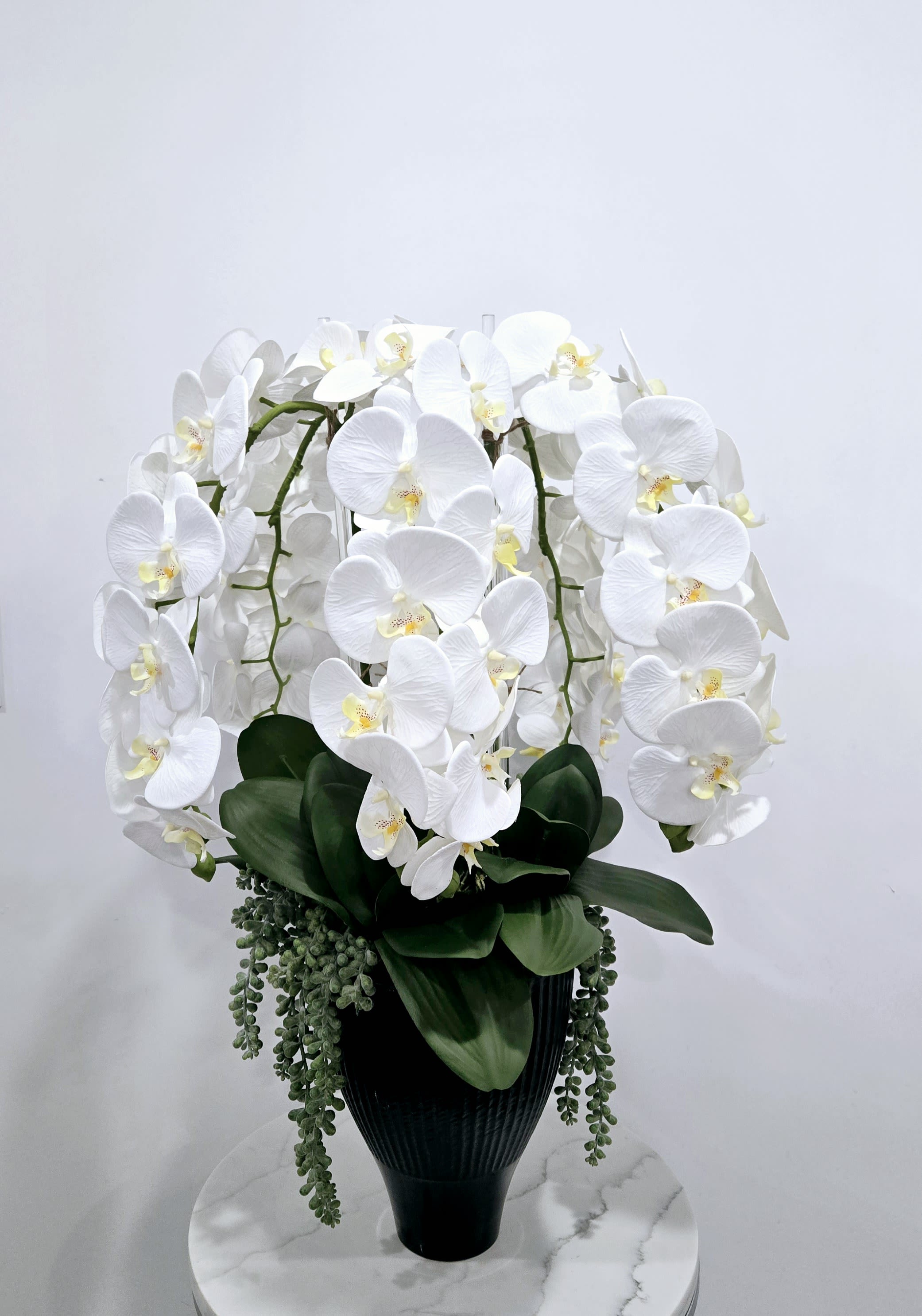 Artificial White Serenity - A beautifully crafted cascade of artificial white phalaenopsis orchids, arranged with lifelike green foliage. This elegant, maintenance-free arrangement adds timeless beauty and tranquility to any interior setting.
