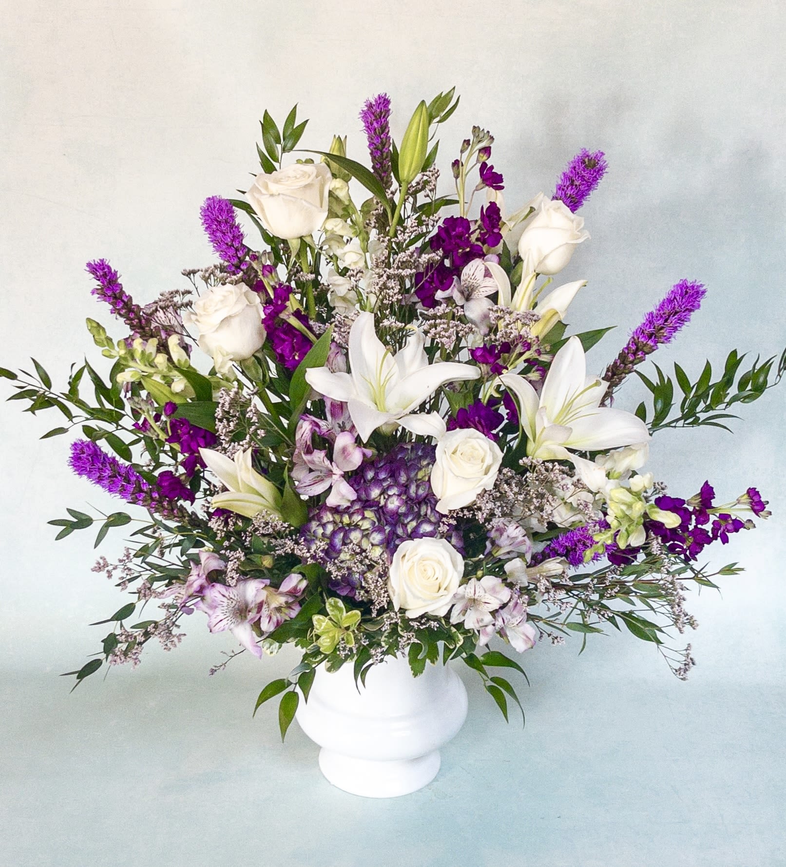 Purple and White Sympathy Arrangement Purple and White Sympathy Arrangement - A tall and one sided arrangement designed for a funeral or memorial service. Seasonal all purple and white flowers make up this beautiful arrangement.