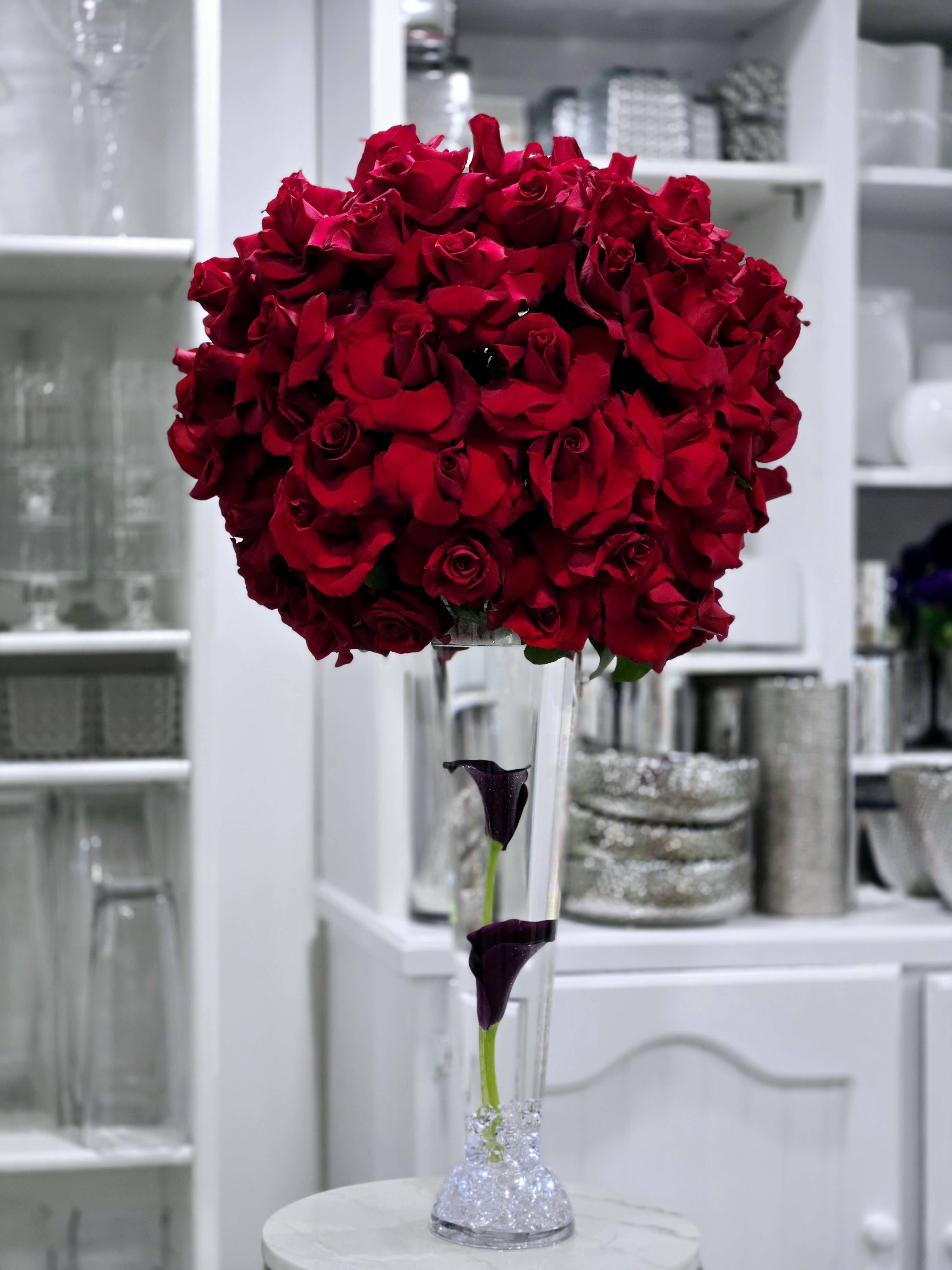 Crimson Majesty - A luxurious dome of red roses atop a sleek glass vase with deep purple calla lilies, creating a bold, elegant centerpiece. Here at Apropos, we design stunning arrangements like Crimson Majesty for all types of events, bringing sophistication and beauty to every occasion. 