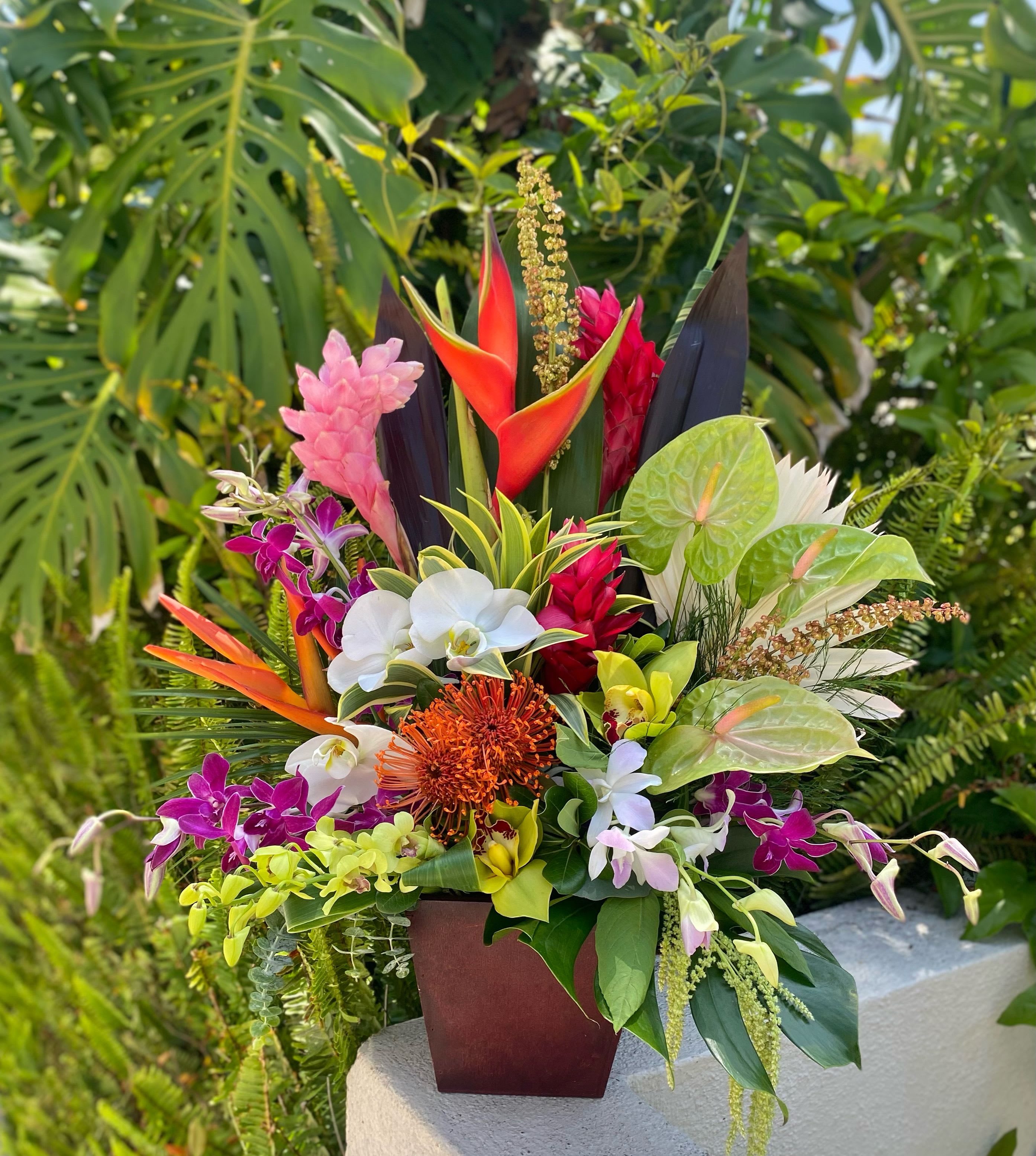 Grand Soleil  - Tropical Flowers beautifully arranged in brown vase with green foliage and variety of orchids. 