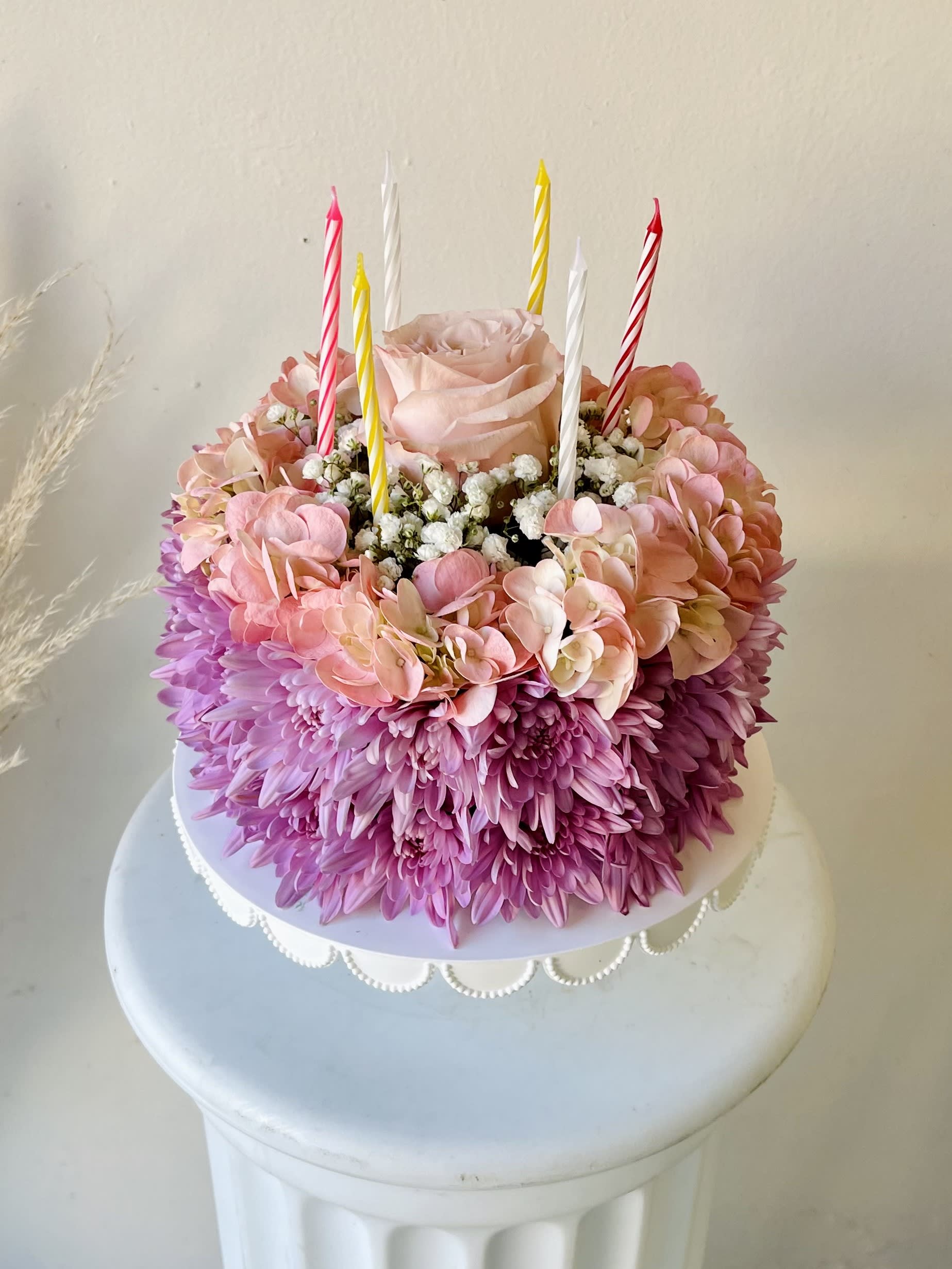  Lovely Pink Birthday Cake - Make their birthday special with this Lovely Pink Birthday Cake.  Arrangement includes lavender chrysanthemums, pink hydrangeas, baby's breath, and a pink rose at the center.  Cake stand and candles are included.  Our florists hand-design each arrangement, so colors and varieties may vary due to availability.