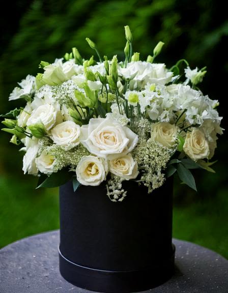 Let Love Grow - This elegant floral arrangement features a luxurious blend of white roses, delicate lisianthus, and lush greenery, arranged in a classic black hatbox. The serene white tones create a perfect for weddings, anniversaries, or any special occasion. Elevate your space with this stunning bouquet,