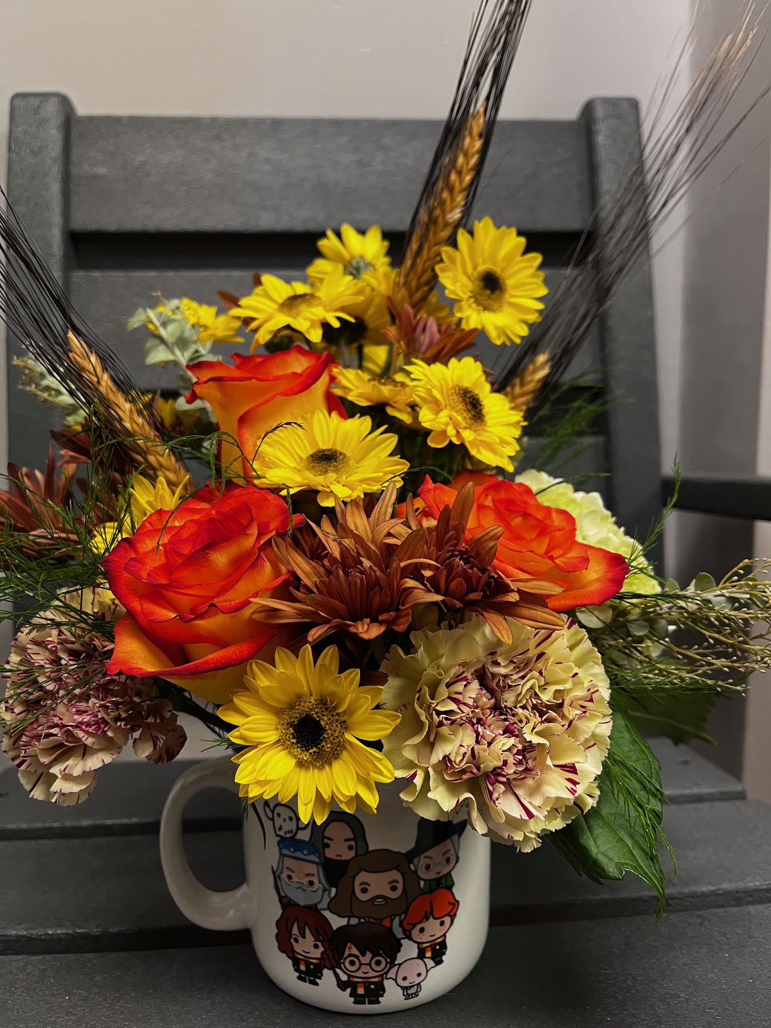Harry Potter Campfire Arangement Harry Potter Campfire Arangement - Experience the magic with our Harry Potter Campfire Mug Arrangement, featuring a machine washable, high-quality mug adorned with vibrant orange roses, yellow and copper daisies, carnations, wheat, and more. This enchanting arrangement is perfect for any Potterhead, combining whimsical floral beauty with practical charm. Ideal for gifting or adding a touch of fantasy to your home decor, this arrangement brings a spellbinding touch to any space.