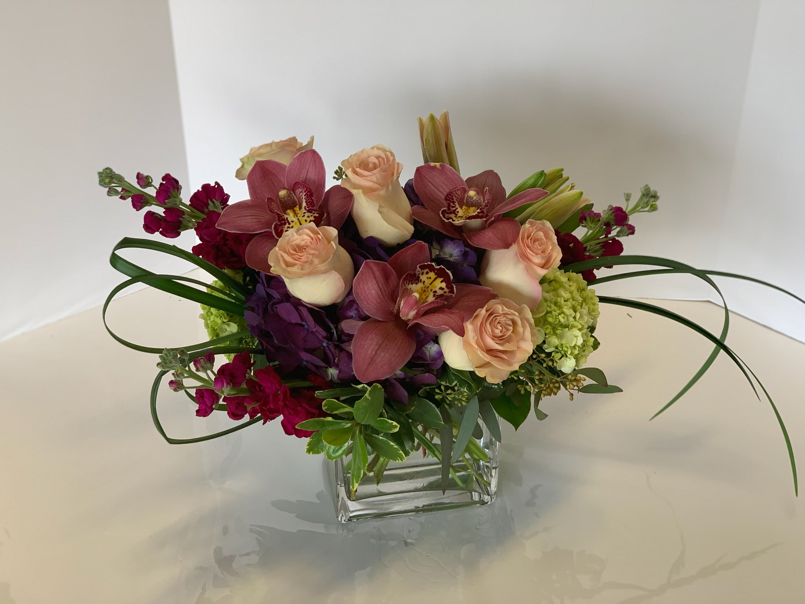 Blush And Burgundy Love Blush And Burgundy Love - Modern rectangle cube of purple with green hydrangea, roses, lilies, stock and cymbidium orchids. Approximately 15" tall by 18" wide