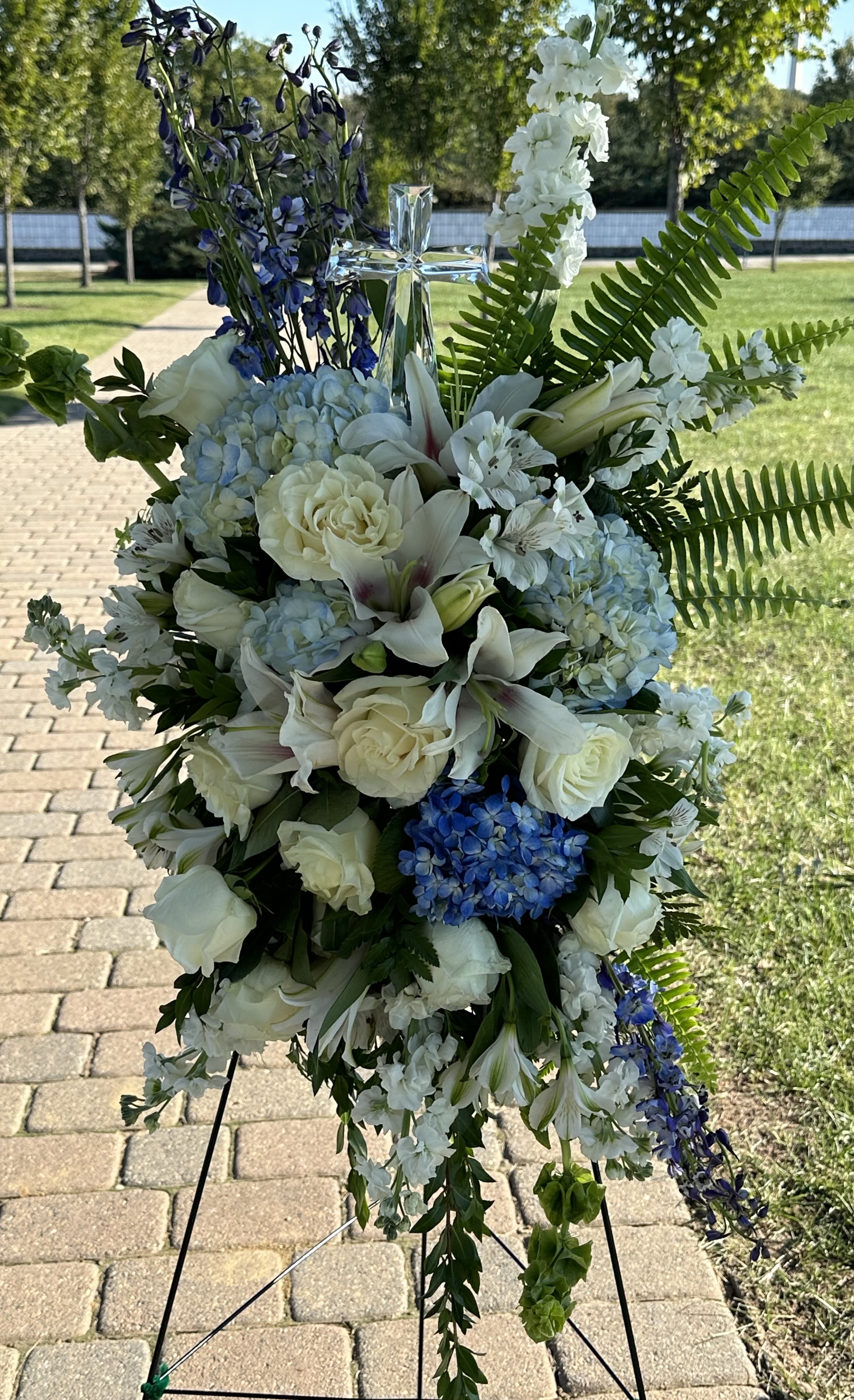 Blue Skies Spray by Petals 2 Go Blue Skies Spray by Petals 2 Go - Our impressive standing spray arrangement, meticulously handcrafted by expert florists with crisp white blooms and rich blue delphinium for a lush, full presentation, creates a proud and respectful commemoration.