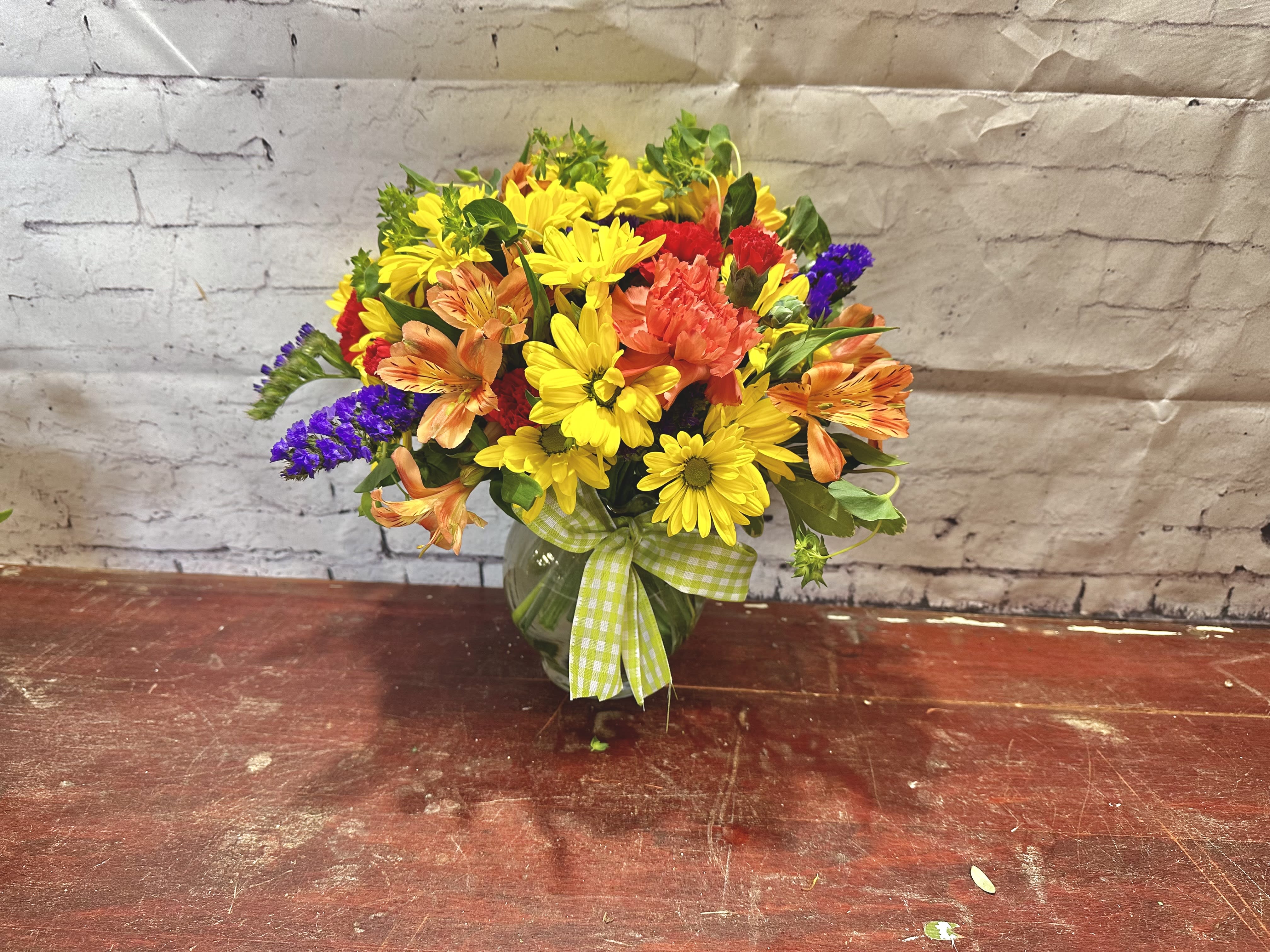 Wishes - A summery mix of yellow daisy chrysanthemums, purple asters and red and orange carnations - arranged in a clear ginger vase and adorned with a cheerful green plaid bow - will make their wishes come true!
