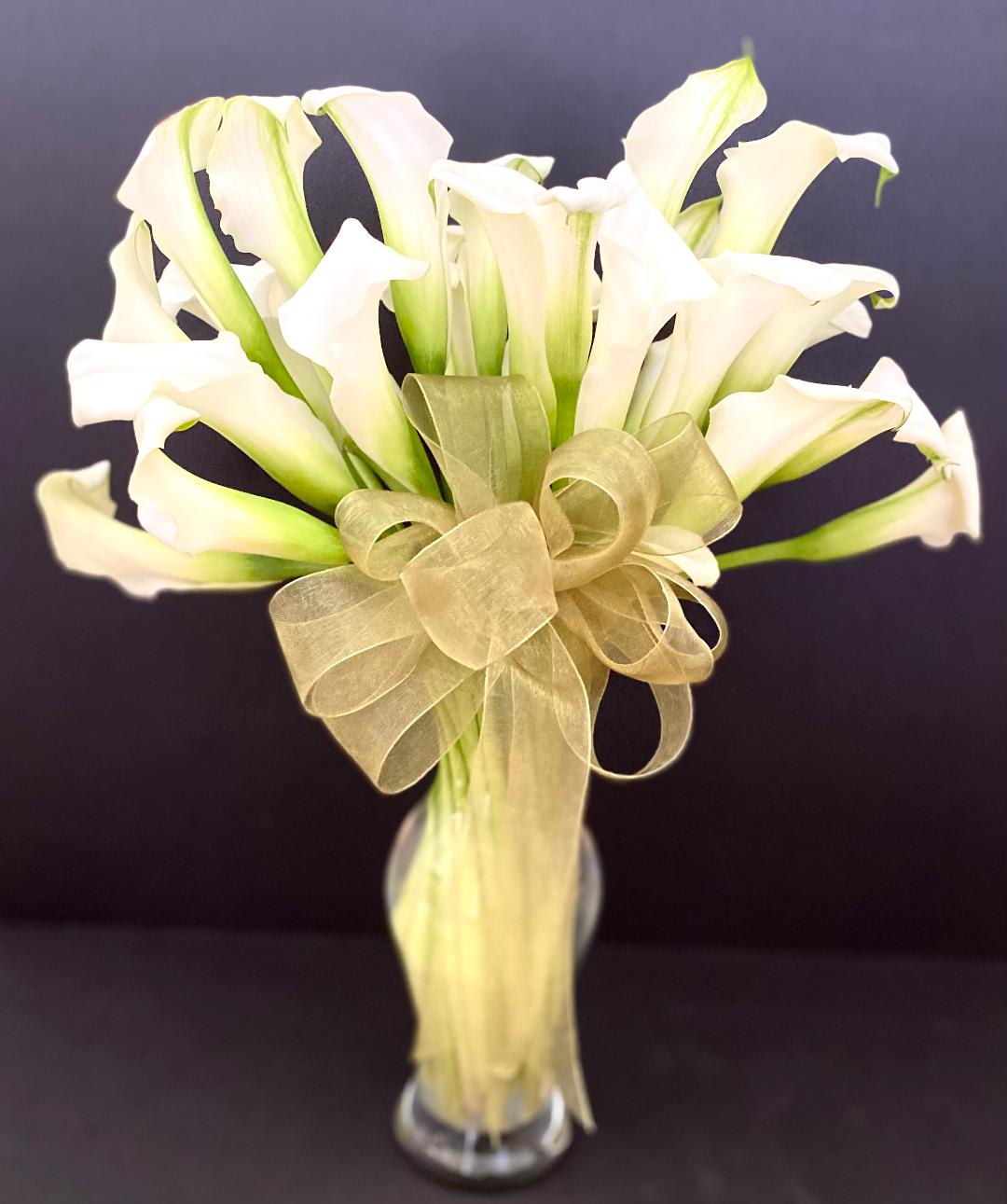 Mini White Calla Lily arrangement Mini White Calla Lily arrangement - This elegant and classic arrangement includes 30 mini White Calla Lilies arranged in a clear vase, accented with a chiffon bow. Perfect for just about any occasion. This design measures approx. 13"w x 18"H.