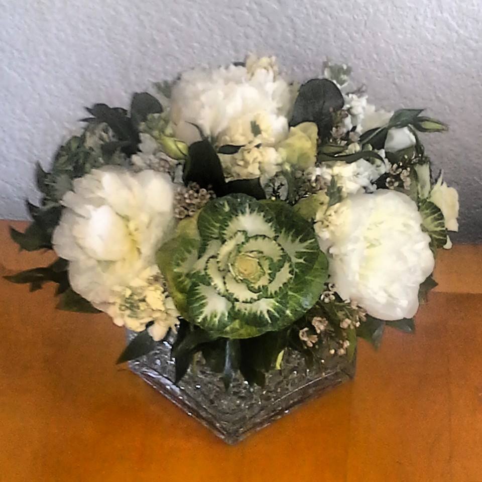 Pretty Peonies Pretty Peonies - An elegant design created for the elegant woman. This design is composed of White Peonies, Kale, Stock, Wax flower, and various foliage set in a glass cube with decorative glass beads lining the cube. This design measures approx. 12"W x 11"H. This design can be created in various colors. Please contact us for details.