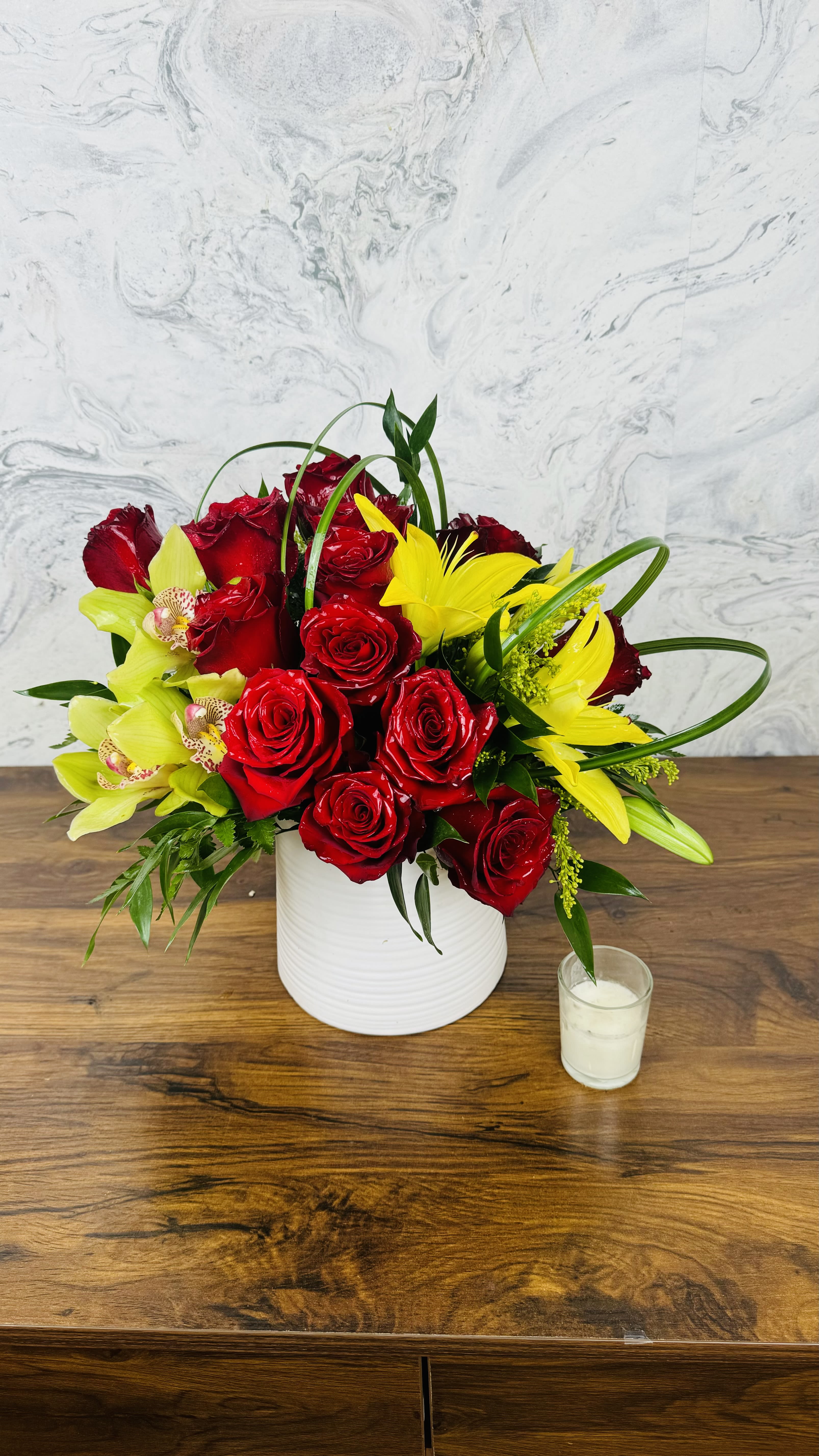 Crimson Radiance - showcases the passionate beauty of red roses, symbolizing love and admiration. Complemented by vibrant yellow lilies that exude warmth and joy, the combination creates a stunning visual contrast. The addition of green orchids introduces an exotic touch, representing strength and luxury. Together, these elements form a captivating display that evokes feelings of romance and celebration, making it perfect for special occasions or as a beautiful gift to convey heartfelt sentiments.