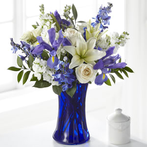 Calming Comfort Bouquet - This handcrafted bouquet of white and blue roses, stock, iris, roses, delphinium, and lilies set in a stunning blue vase offer your loved ones comfort and support in their time of need.