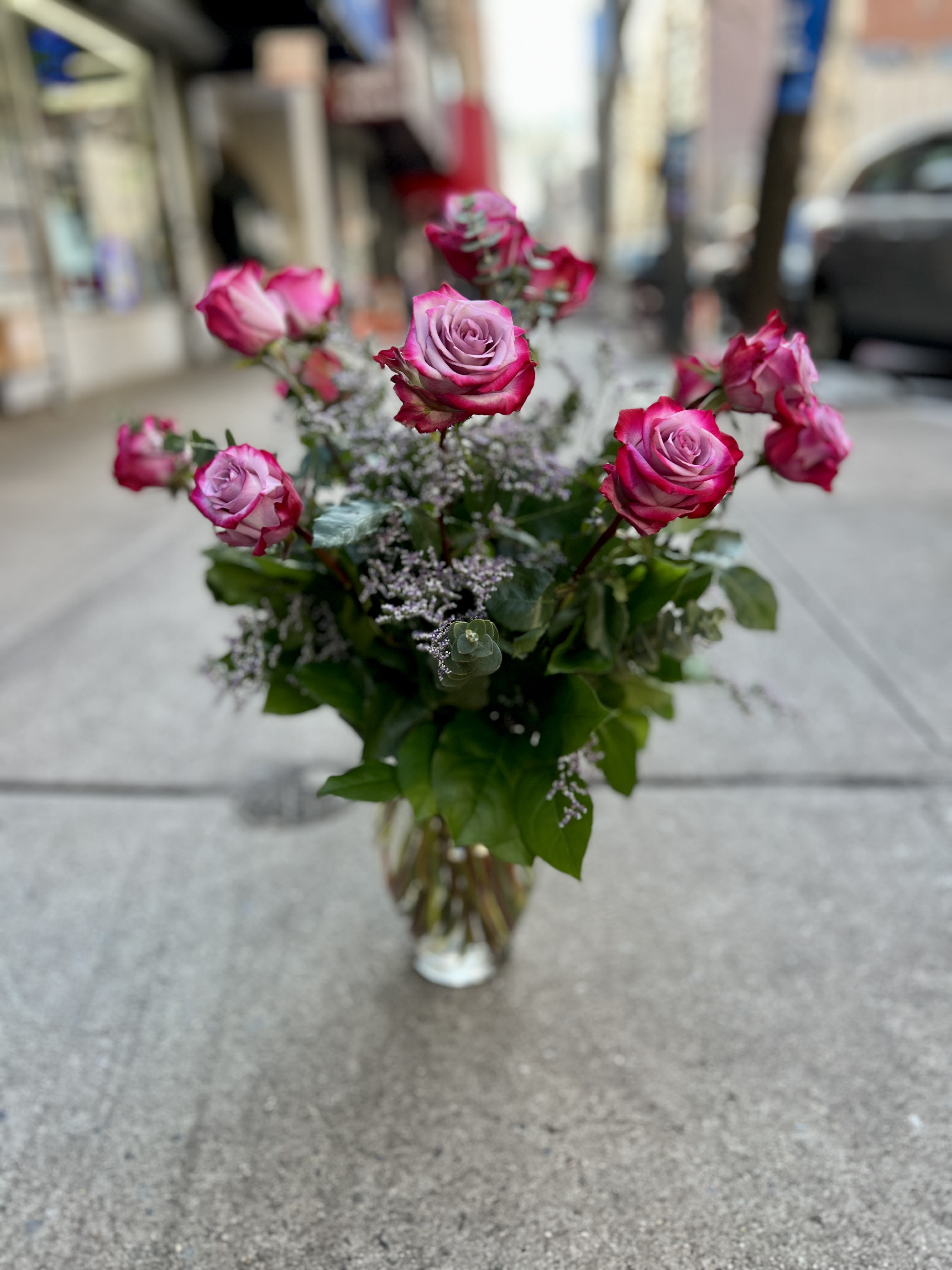 One Dozen Deep Purple Roses  - CLASSIC ROSES BY THE DOZEN! DESIGNED IN A TALL VASE TO SHOW OFF THE LONG STEMS OF A CLASSIC “LONG STEM ROSE” ARRANGEMENT. WE USE GREENERY AND SOME PETITE FILLER FLOWERS OR BRANCHES TO GIVE YOUR ROSES EXTRA VOLUME THAT MAKE A HUGE IMPACT.CLASSIC ROSES BY THE DOZEN! DESIGNED IN A TALL VASE TO SHOW OFF THE LONG STEMS OF A CLASSIC “LONG STEM ROSE” ARRANGEMENT. WE USE GREENERY AND SOME PETITE FILLER FLOWERS OR BRANCHES TO GIVE YOUR ROSES EXTRA VOLUME THAT MAKE A HUGE IMPACT.If your special someone isn't a fan of red roses brighten their day with these stunning Deep Purple roses! These two tone magenta and lavender beauties are sure to make them smile on Valentine's Day or for any special event in your life! 