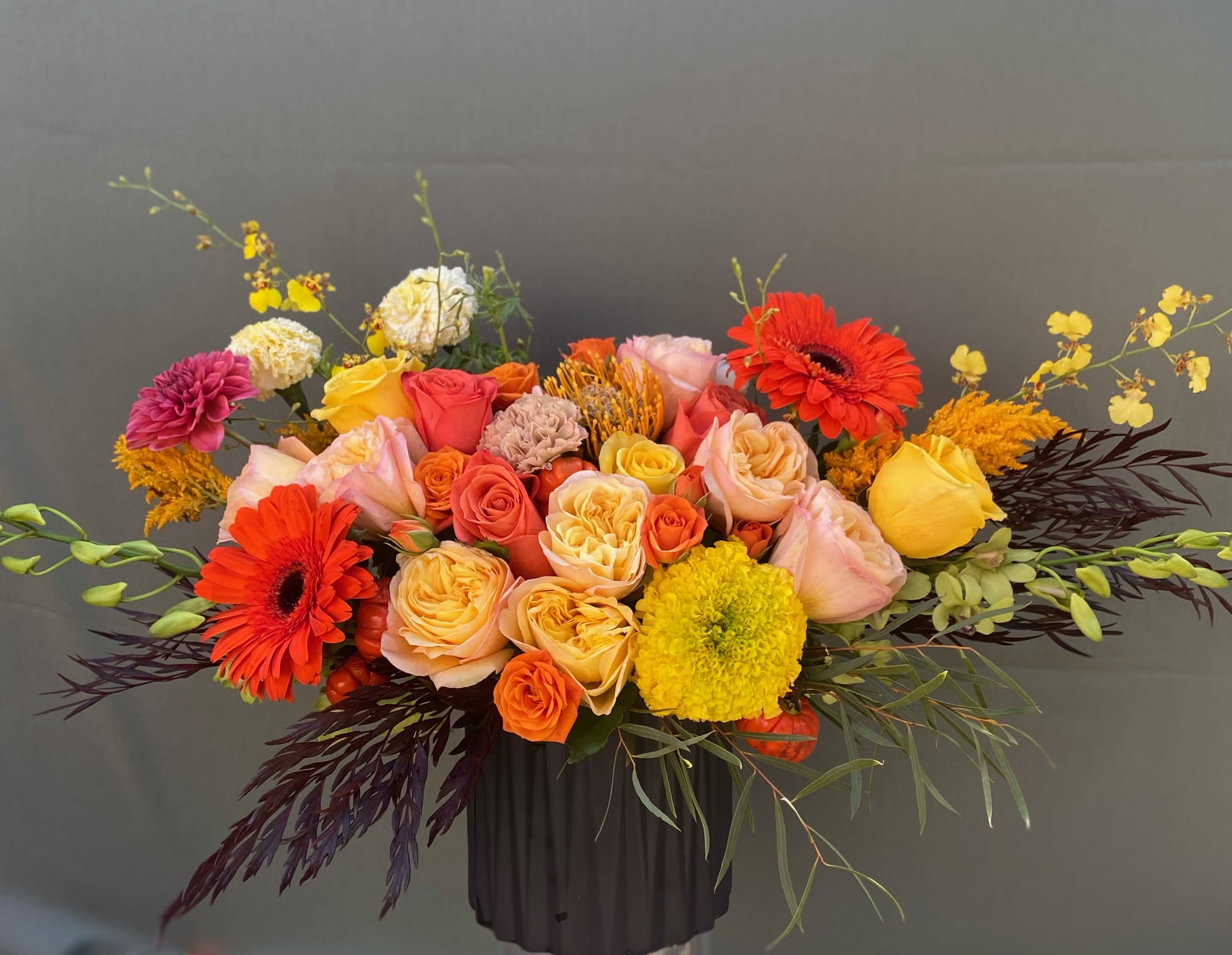 Honey Autumn - This arrangement includes marigolds, gerberas, roses, dendrobium orchids, dahlias, with green foliage all arranged in ceramic vase.