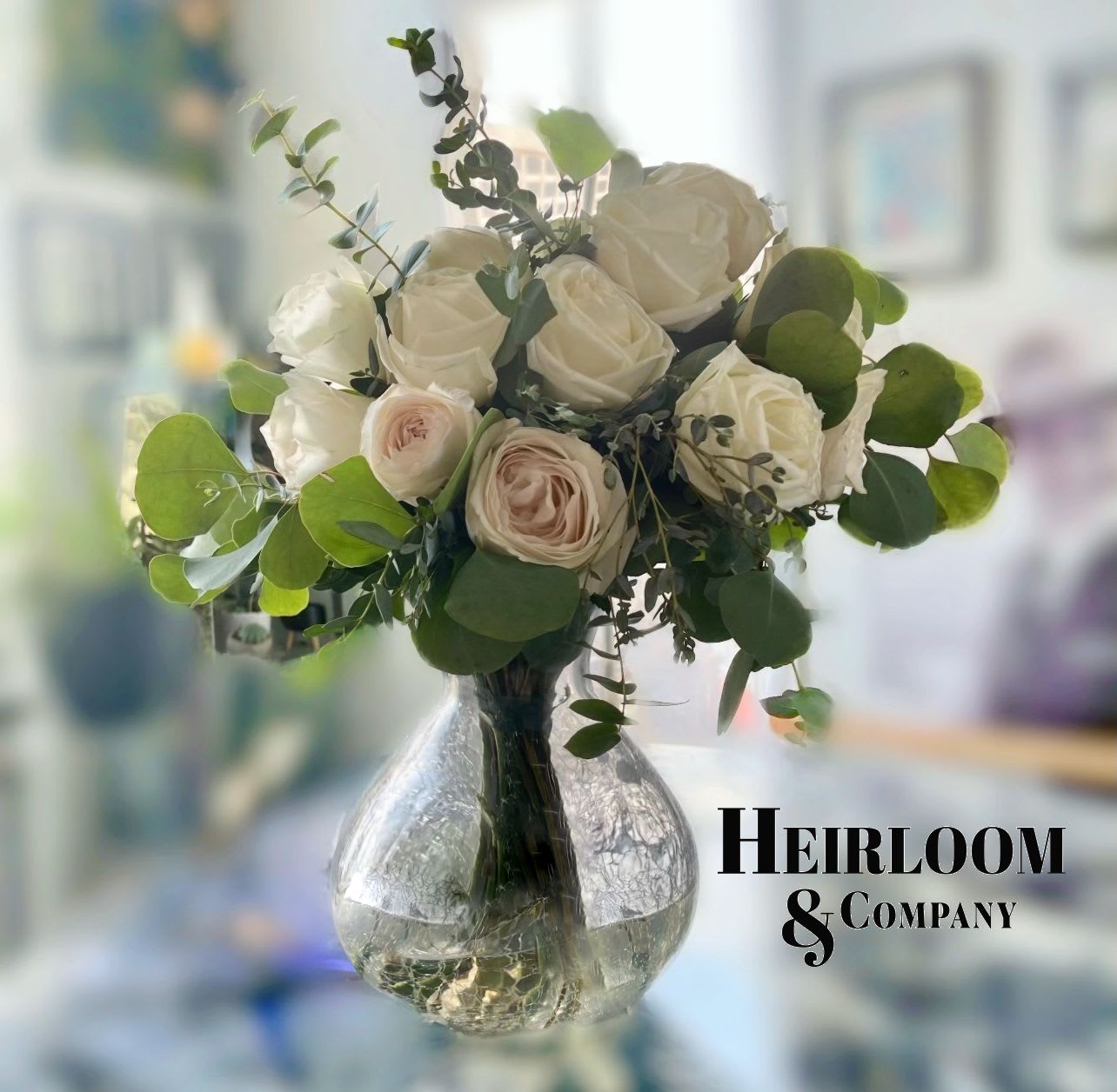 White Roses and Eucalyptus White Roses and Eucalyptus - Premium white garden roses paired with the elegance of several varieties of dusty colored eucalyptus in a very modern crackle glass vase.