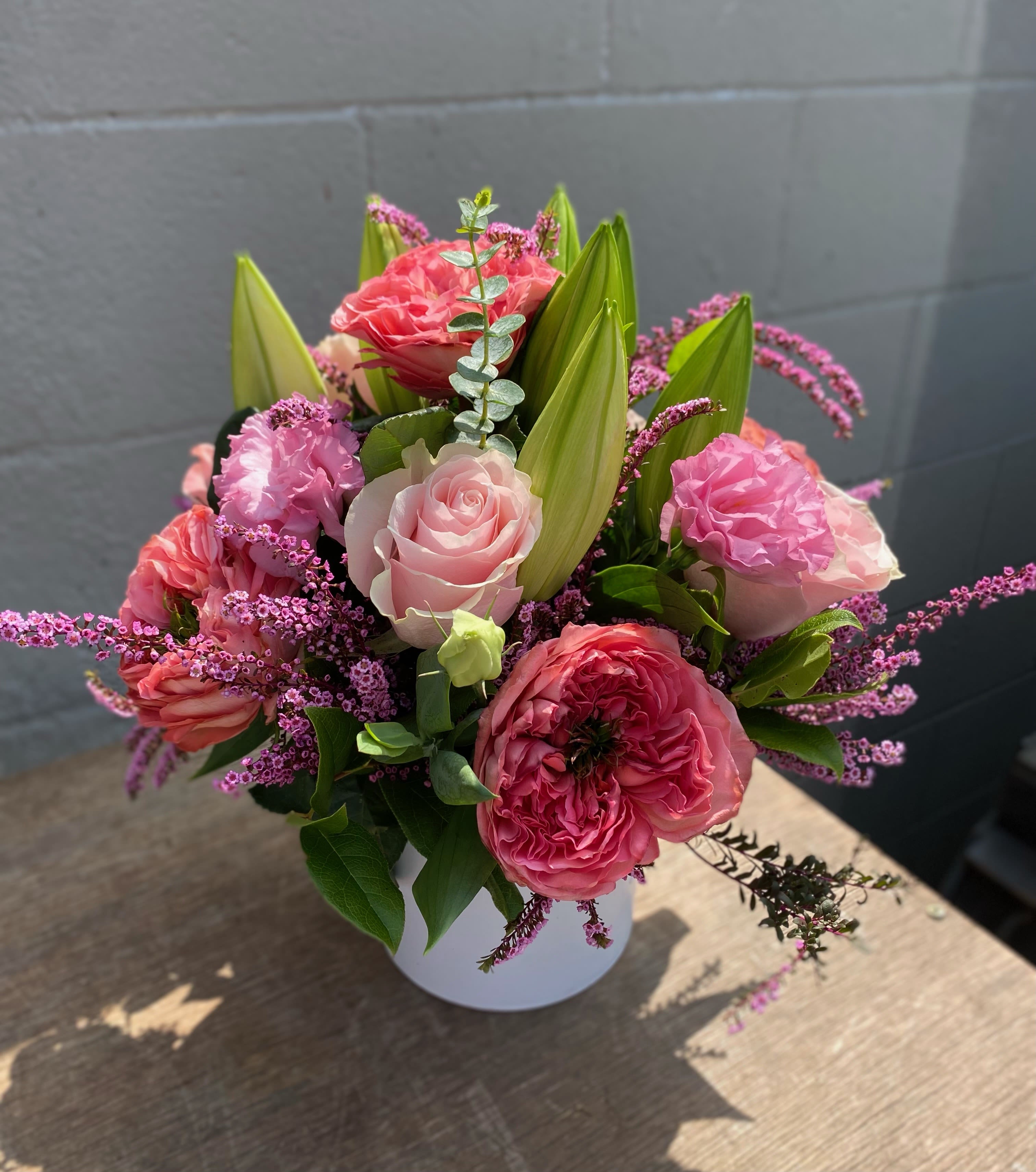 She  - This arrangement includes garden roses, lilies, green foliage all hand arranged in white ceramic vase. 