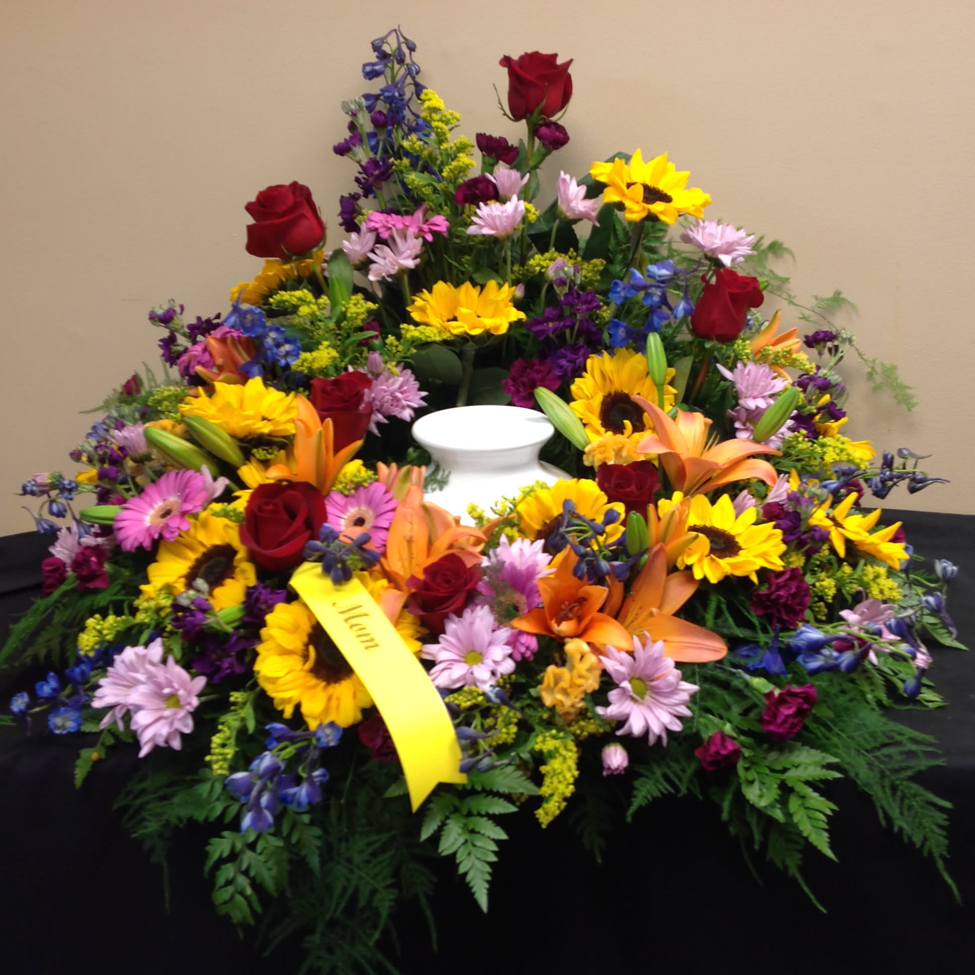 Happy Memories Urn Wreath - An urn wreath created with a vibrant garden-like mixture of flowers including:  sunflowers, orange Asiatic lilies, fuschia mini gerbera daisies, deep blue delphinium, and red roses. 
