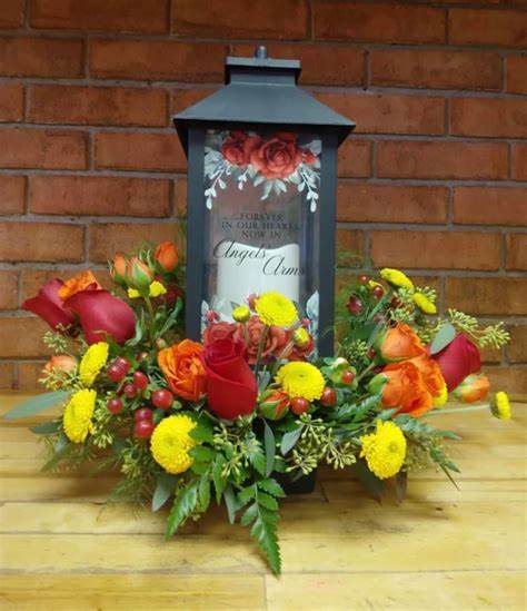 Angel Arms Lantern with Fresh Flowers Angel Arms Lantern with Fresh Flowers - Forever in Our Hearts Lantern with fresh flowers. These lanterns are made of weather friendly materials and UV printed glass. They include a flameless LED candle with a built-in automatic timer: 6hrs ON/18hrs OFF (3 AAA batteries are included). They are suitable for hanging or free-standing use. W: 5.5" H: 13" D: 5.5"