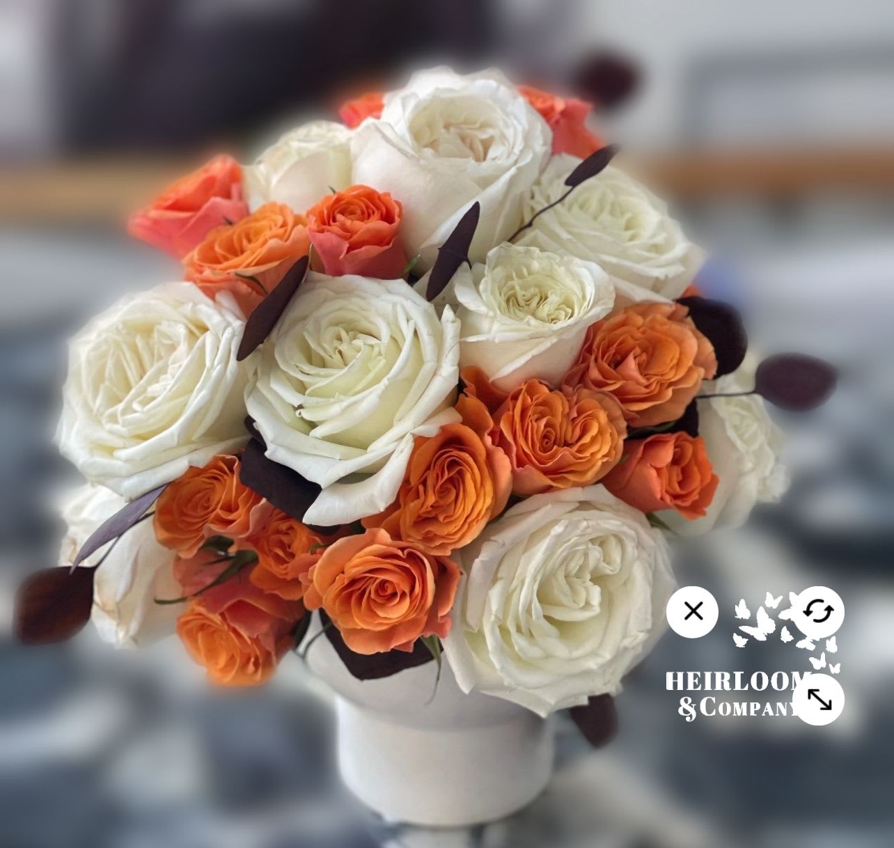 The thanksgiving Arrangement - Our most premium white garden roses, burgundy eucalyptus, and sunshine orange spray roses presented in a modern style white ceramic bowl. Perfect for your home or as a gift to any holiday event you attend!
