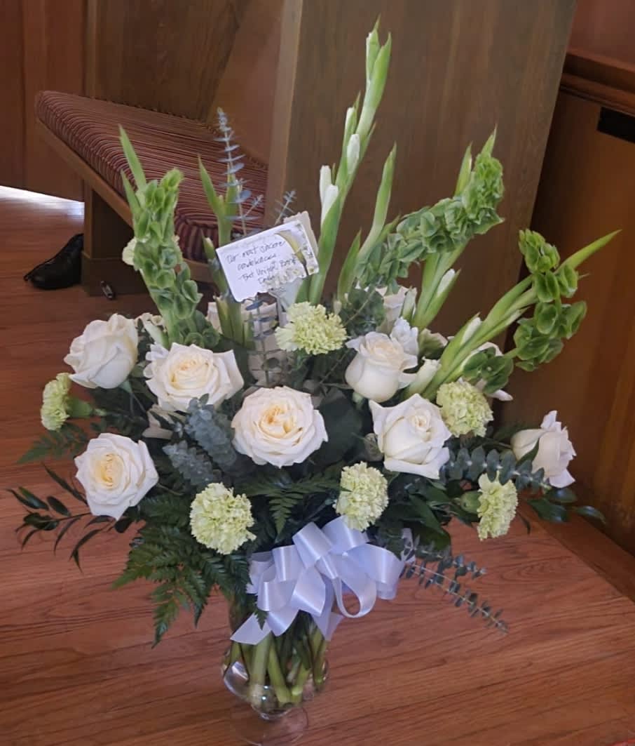 Celebration of Life Vase - A Graceful, Elegant, and Respectful Celebration of Life piece.  The magnificent white roses, Bells of Ireland, stunning Snap Dragons, and glimmering green carnations radiate peace, admiration, and remembrance. Top choice for a memorable memorial.