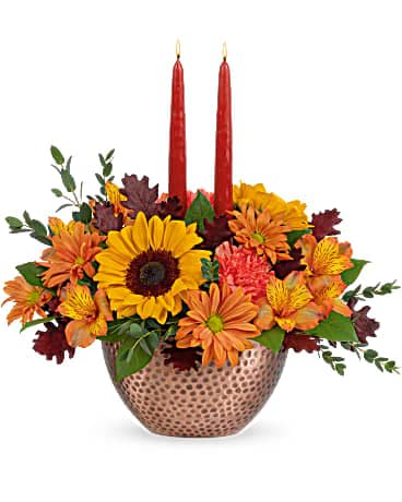 Teleflora's Autumn Copper Centerpiece - Like a fall sunrise, this heart-warming centerpiece brightens any room with its sunny blooms, glowing tapers and gorgeous hammered, copper-hued bowl. This stunning centerpiece features medium yellow sunflowers, orange carnations, bronze daisy spray chrysanthemums, orange alstroemeria, parvifolia eucalyptus and lemon leaf, accented with preserved oak leaves and candles. Delivered in a Copper Beauty bowl.