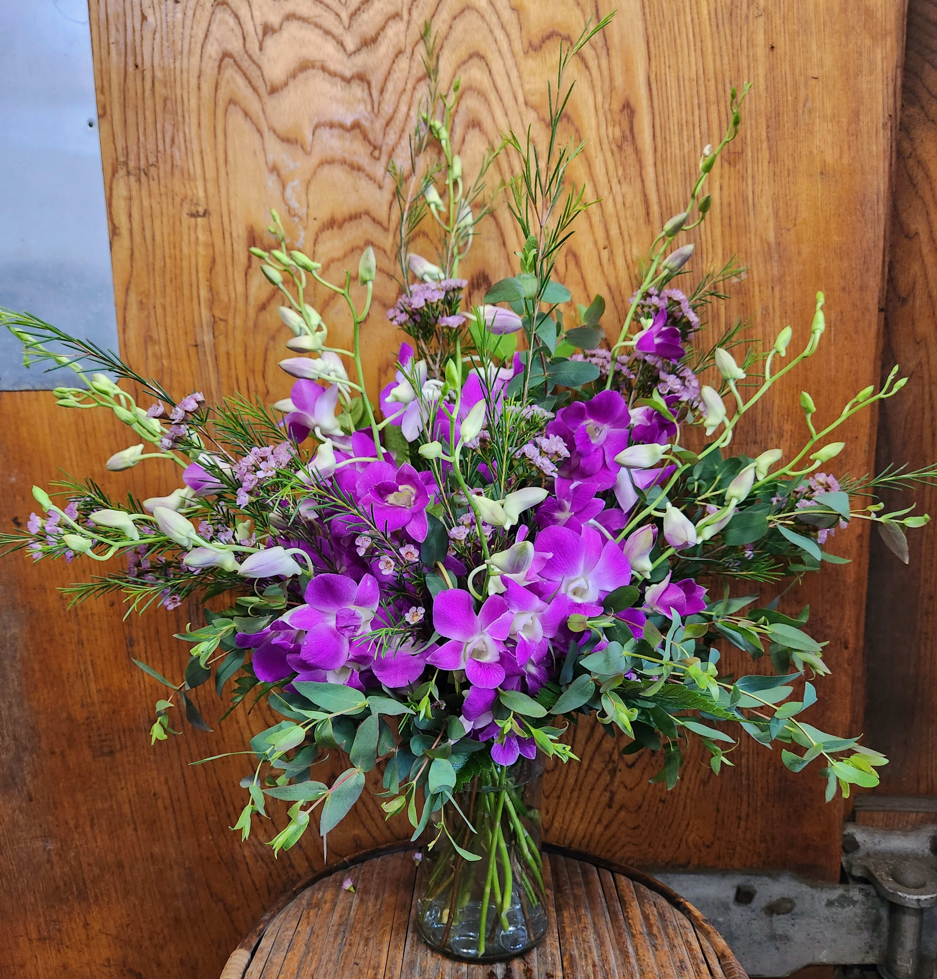 Dendrobium Daze Dendrobium Daze - A full bunch of 10 stems of Dendrobium orchids, bursting from a tapered glass vase. Accented with eucalyptus and waxflower. A simple and elegant presentation that suits both everyday and special events.