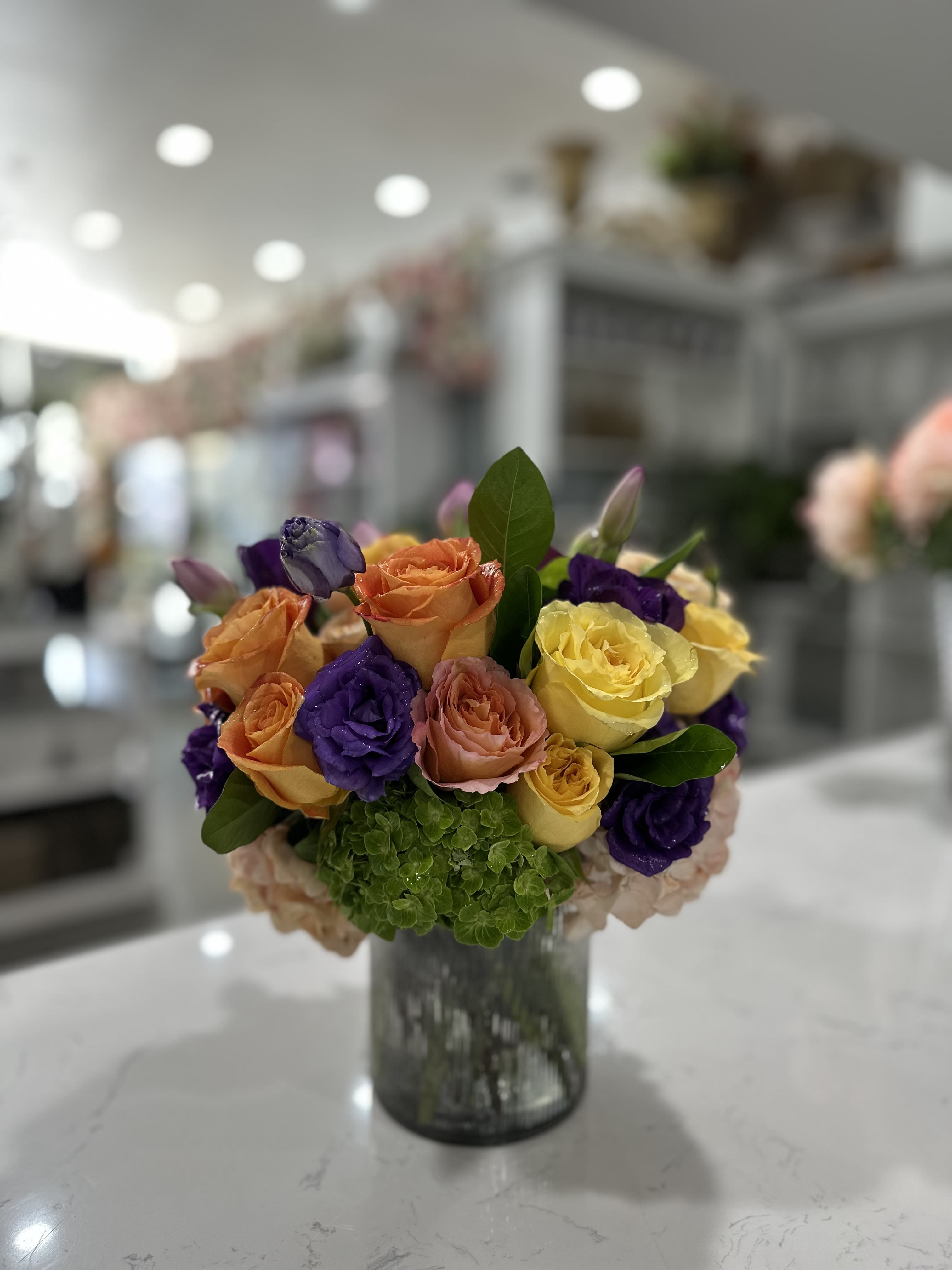 Sunset Symphony - A harmonious blend of vibrant orange, purple, and yellow roses, paired with lush green hydrangeas. This modern arrangement is perfect for adding a colorful touch to any setting.