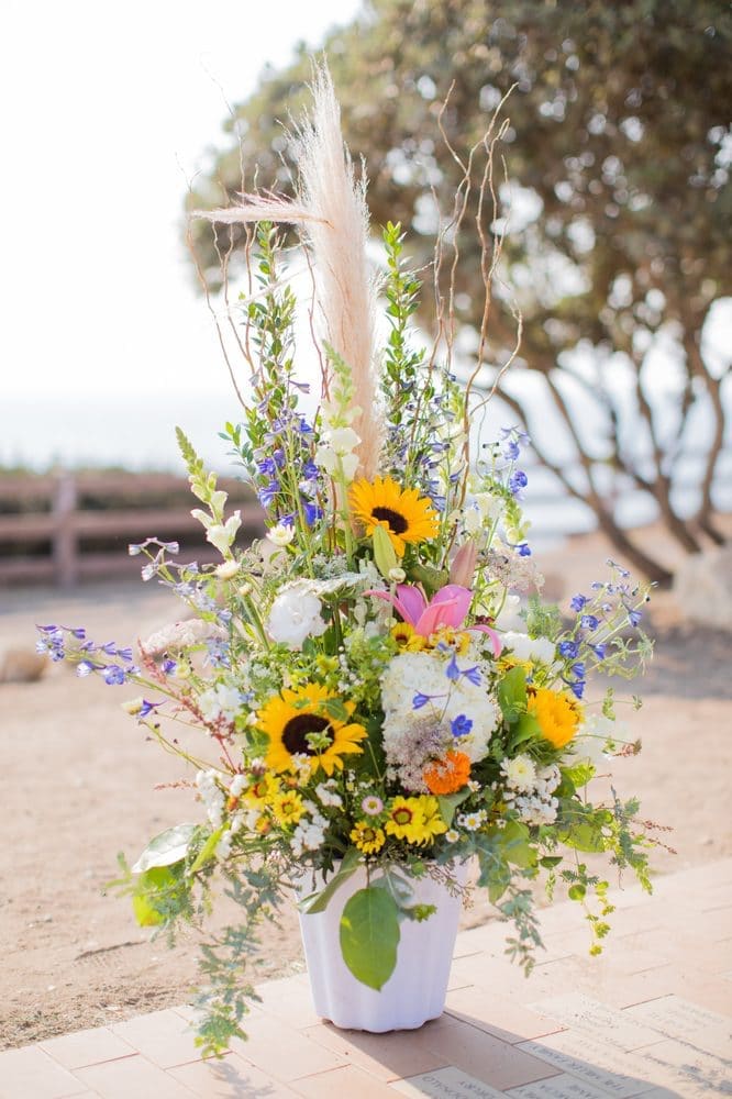 Wild Wishes Wild Wishes - Beautiful wild flowers, daisies, sunflowers, snapdragon, and much more arranged in a white vase.