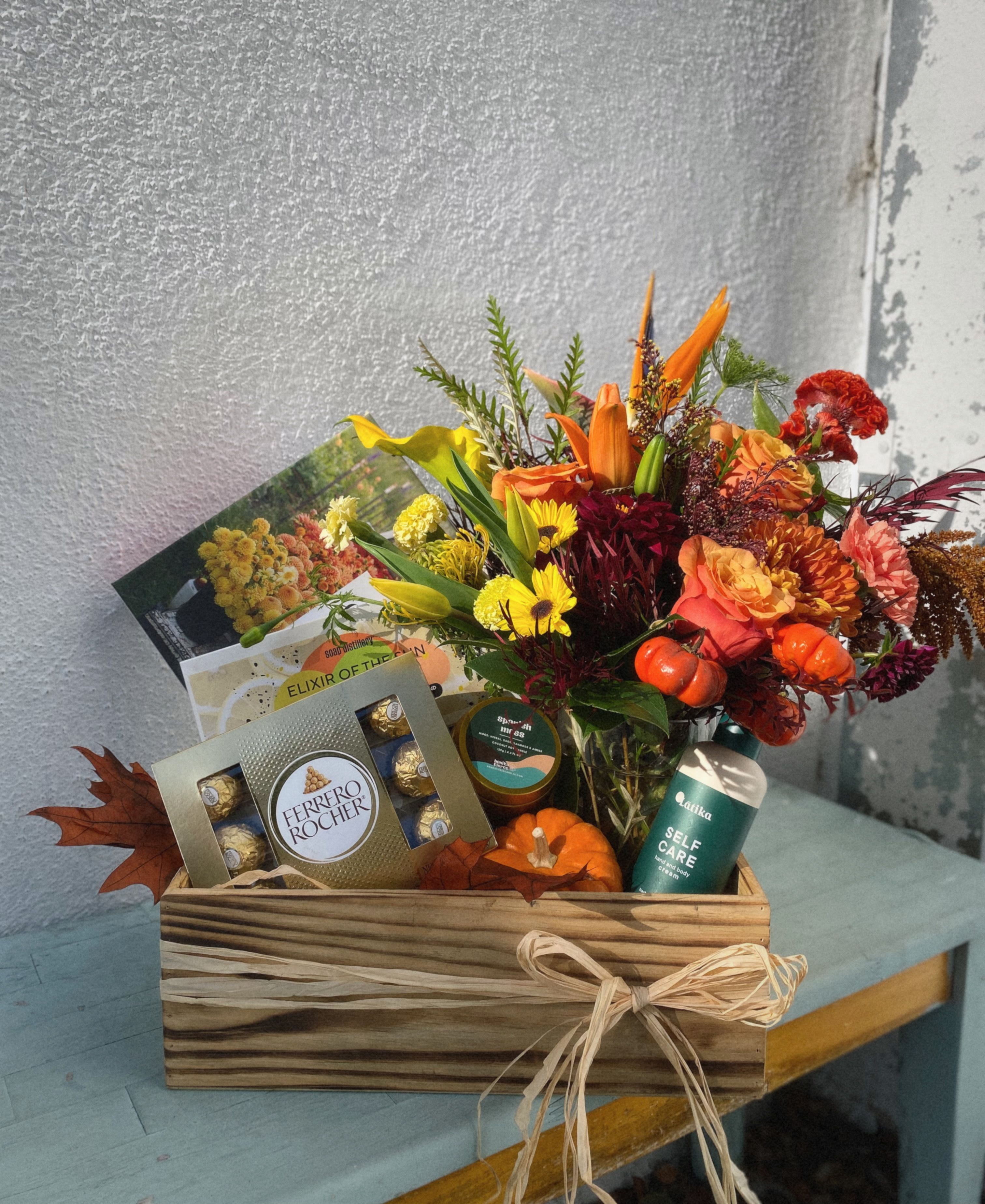 Cozy Autumn Crate - This charming gift box features a beautiful flower arrangement fill with a variety of fall flowers. It also includes Latika hand and Body cream, Bonita Fierce Coconut soy candle,  bar soap gift set ferrero chocolates, a 500 piece floral puzzle, and a small decorative pumpkin-perfect for a cozy fall self-care night!